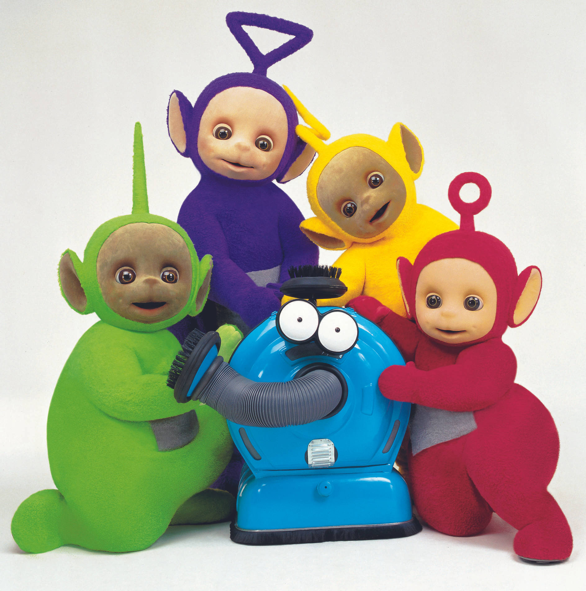 Teletubbies 桌布 壁紙 — 四個色彩繽紛的天線寶寶穿著毛絨服裝，圍繞著一個有咕嚕眼睛的藍色吸塵器，背景是純白色。