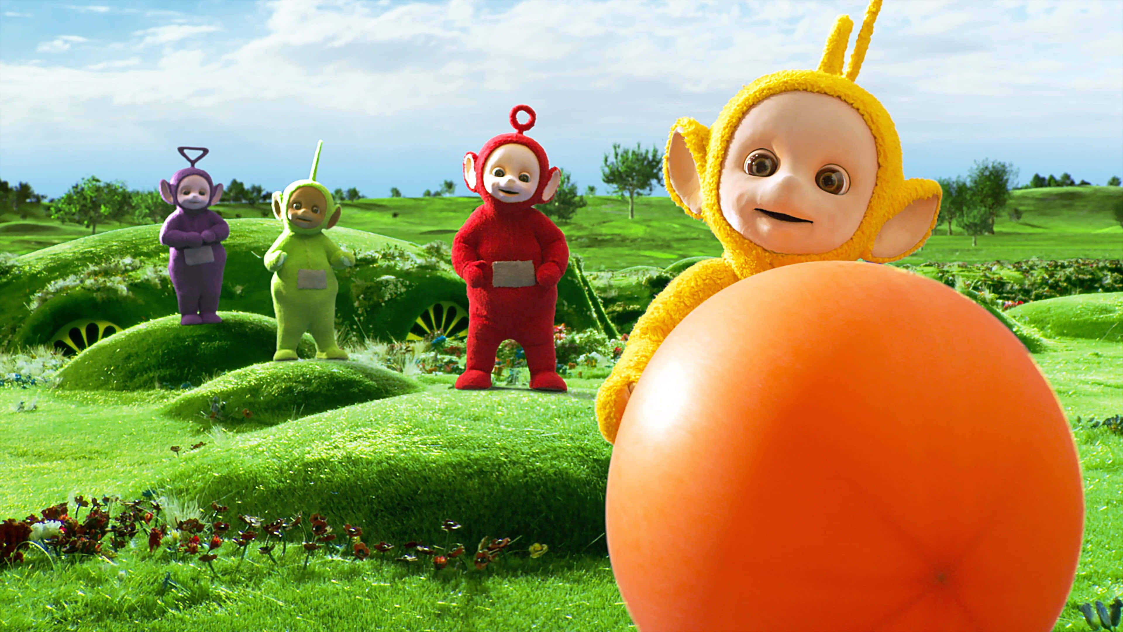 Teletubbies 桌布 壁紙 — 四個色彩繽紛的天線寶寶站在一個充滿活力的綠色起伏草地上，天空湛藍，白雲朵朵。