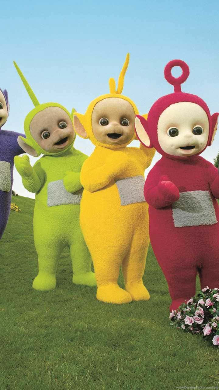 Teletubbies 桌布 壁紙 — 四個色彩繽紛的天線寶寶站在長滿草的山丘上，藍天白雲，附近有花叢。