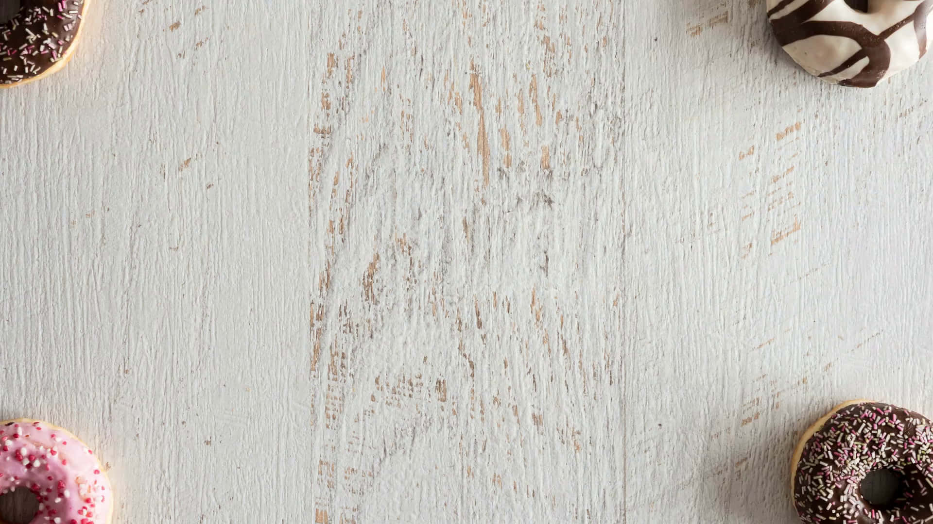 White Wood 桌布 壁紙 — 四個色彩繽紛的甜甜圈，上面有糖粒和巧克力淋醬，圍繞著一個風化的白色木質表面。