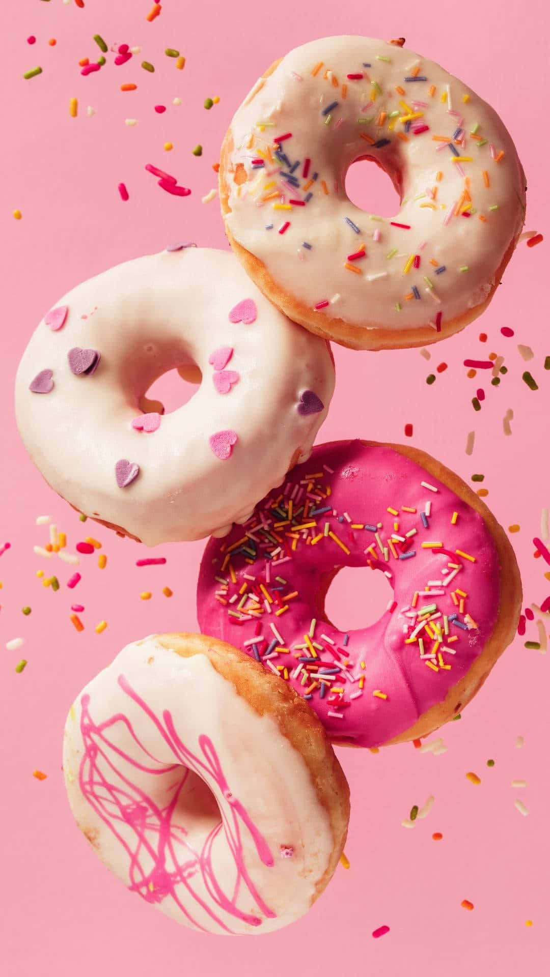Cute Donut 桌布 壁紙 — 四個色彩繽紛的甜甜圈灑上糖針，在柔和的粉紅色背景上漂浮，構成有趣的畫面。