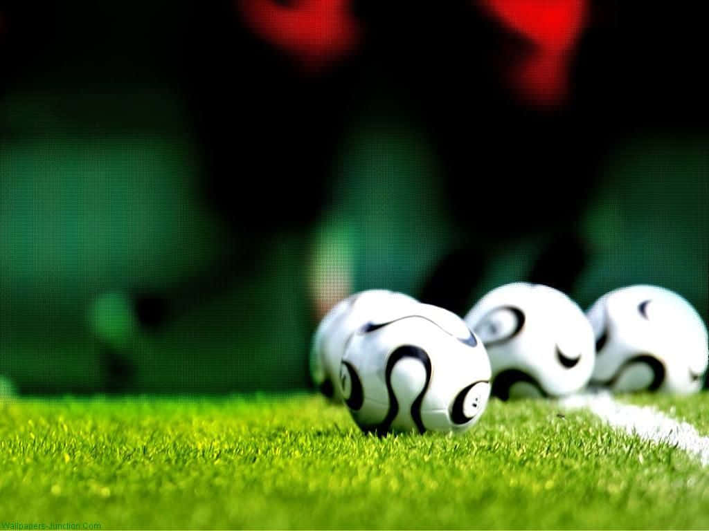 Soccer 4K 桌布 壁紙 — 四個足球放在充滿活力的綠色草地上，背景是模糊的體育場。