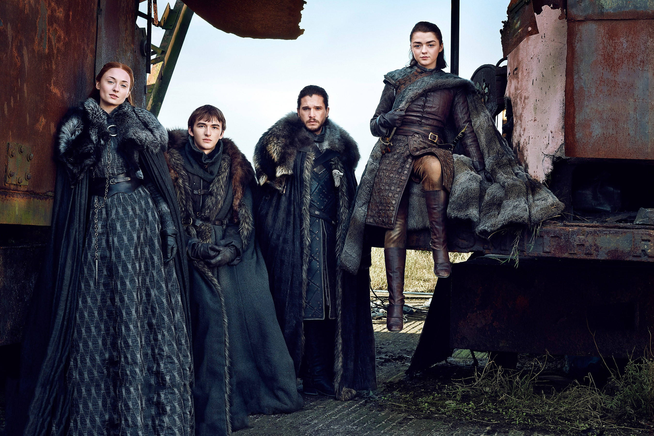 Sansa Stark 桌布 壁紙 — 四個身穿毛皮襯裡斗篷的裝甲人物，在荒涼的戶外環境中莊嚴地站在一個生鏽的金屬結構旁。
