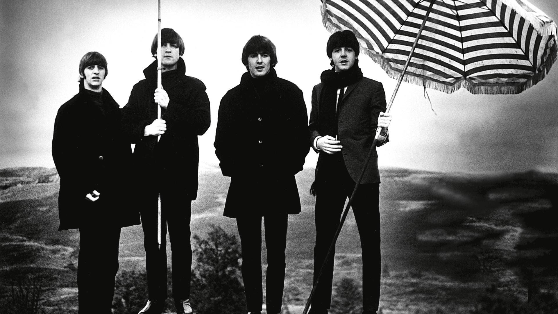 the beatles 桌布 壁紙 — 四個身穿深色大衣的男人站在山坡上，撐著傘對著多雲的天空。