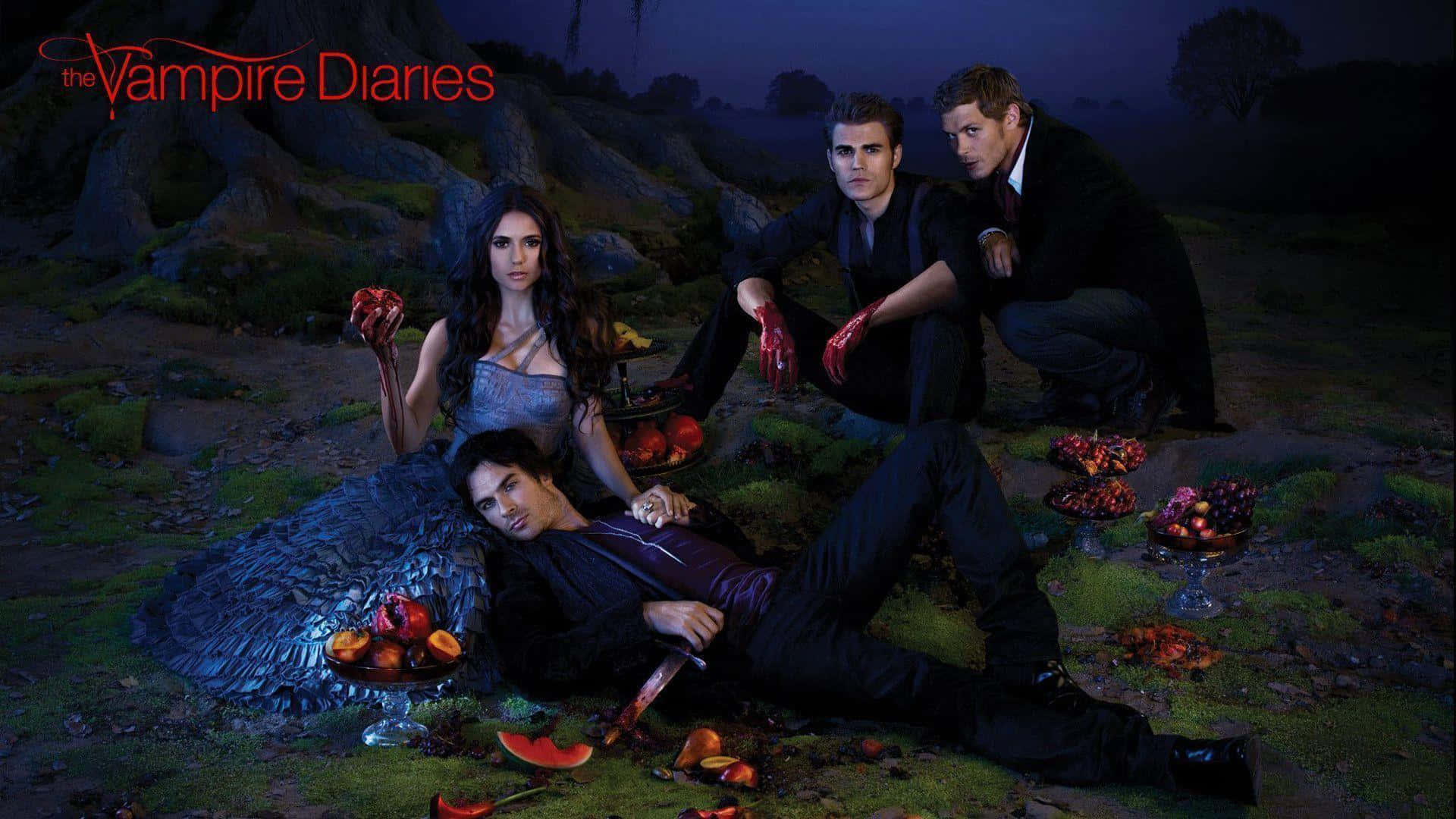 Vampire Diaries Desktop 桌布 壁紙 — 四個身穿深色服裝的吸血鬼在月光照耀的森林空地中戲劇性地擺姿勢，周圍環繞著血淋淋的水果和發光的藍色翅膀。