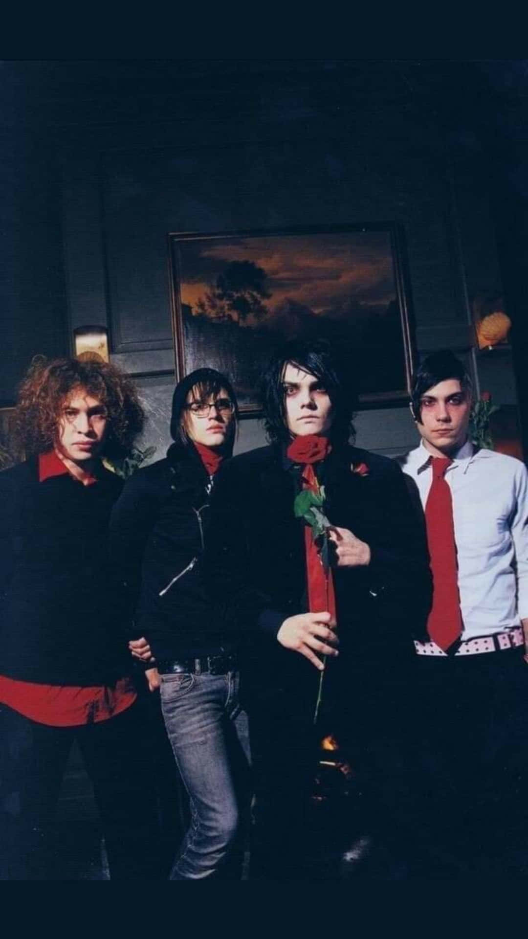 emo 桌布 壁紙 — 四個身穿深色衣服帶紅色點綴的男人在昏暗的房間裡莊嚴地擺姿勢，手持一朵紅玫瑰。