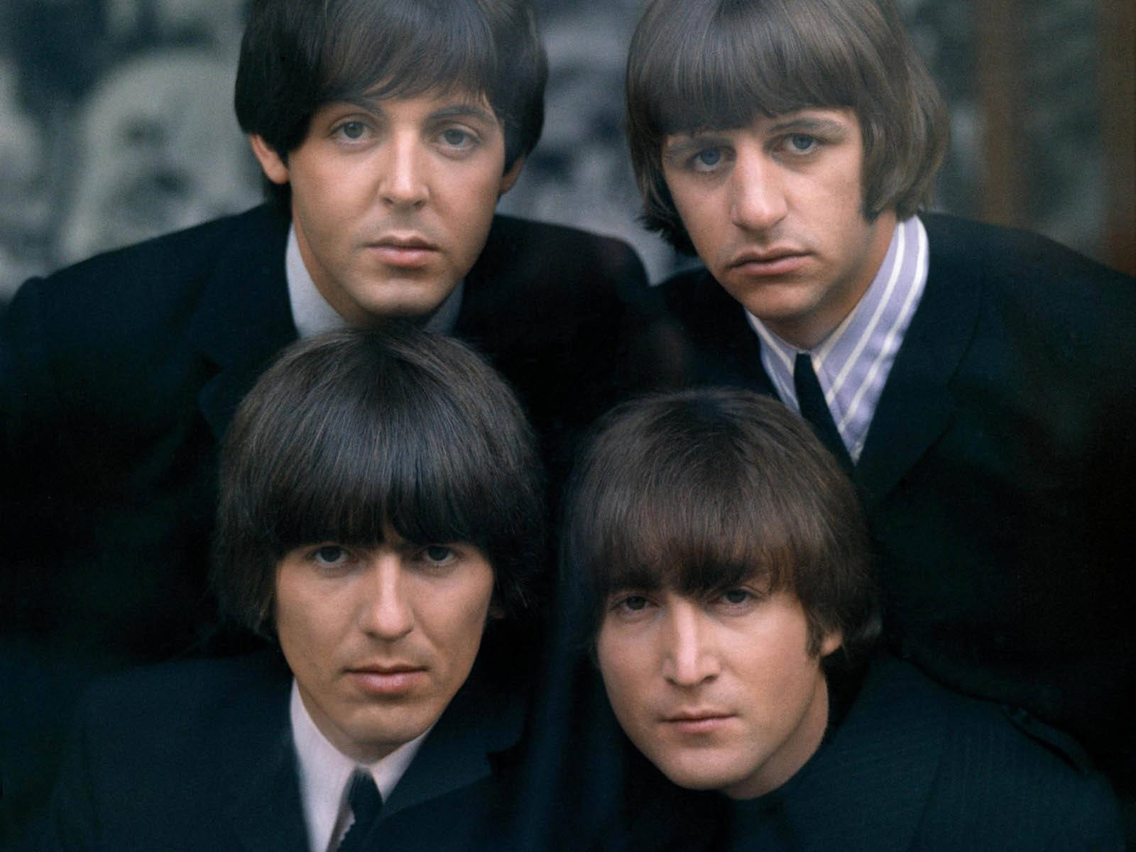 the beatles 桌布 壁紙 — 四個身穿深色西裝、表情嚴肅的男人，在模糊的背景前直視鏡頭。