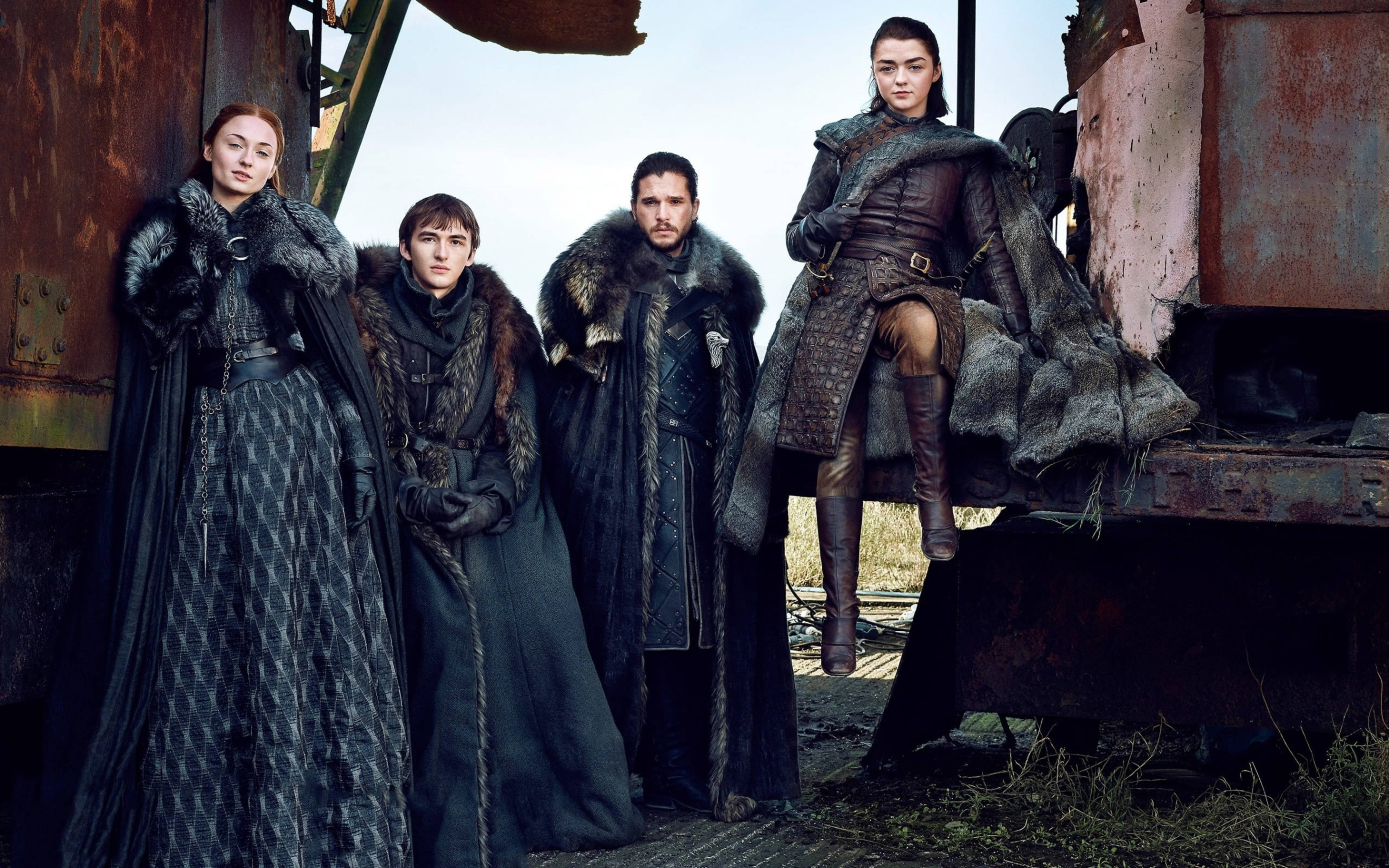 House Stark 桌布 壁紙 — 四個身穿鎧甲、披著毛皮襯裡斗篷的人物，莊嚴地站在荒涼田野中生鏽的火車車廂旁。
