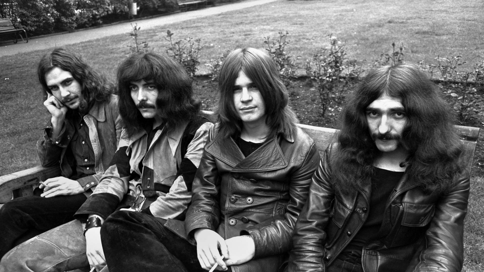 Ozzy Osbourne 桌布 壁紙 — 四個長髮男子穿著皮夾克，表情嚴肅，叼著煙，黑白風格坐在公園長椅上。