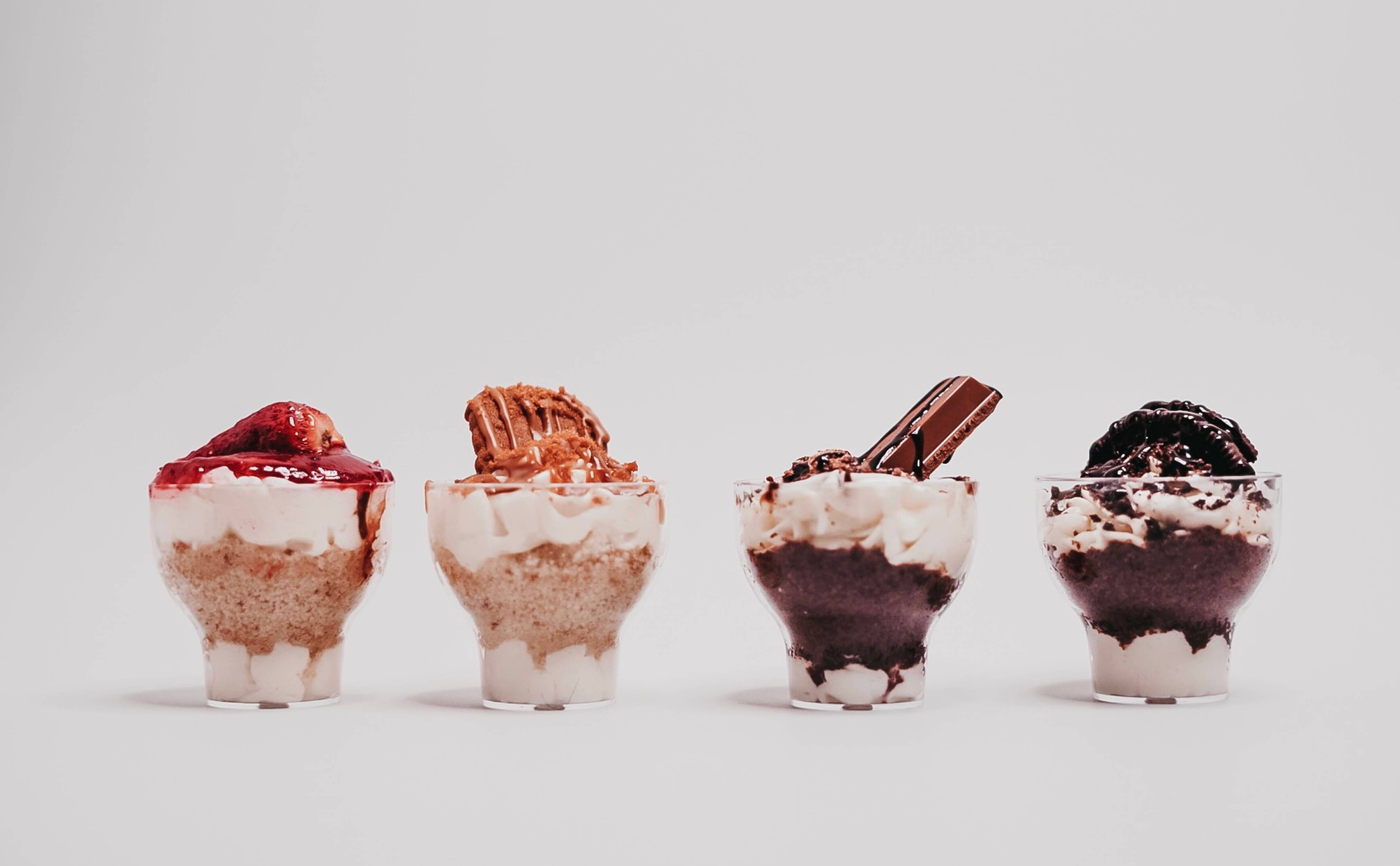 Ice Cream 桌布 壁紙 — 四個頹廢的甜品杯，上面有各種配料，整齊地排列在純白色背景上。
