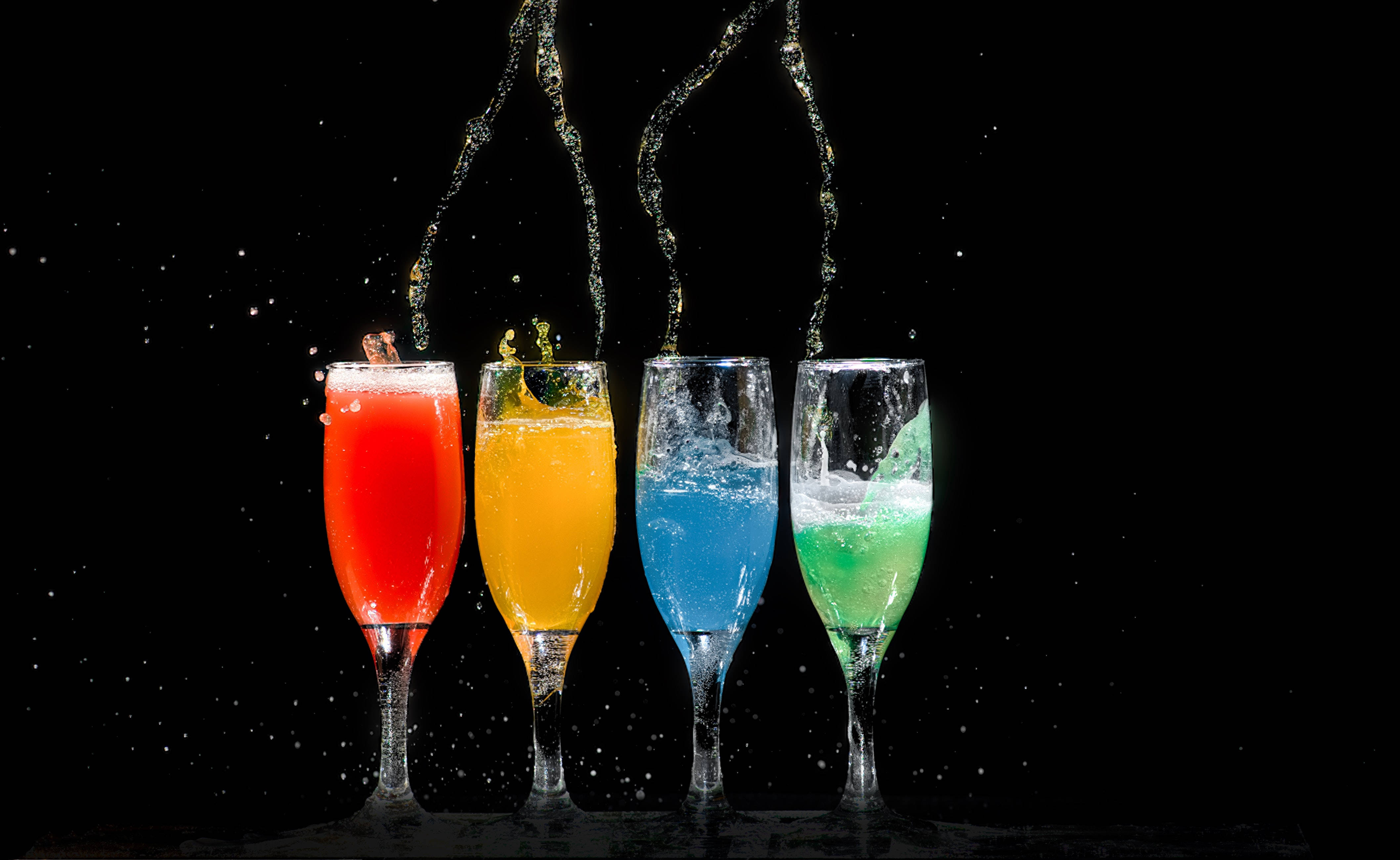Drink 桌布 壁紙 — 四個香檳杯盛滿鮮豔的紅、黃、藍、綠色飲料，在黑色背景上戲劇性地飛濺。