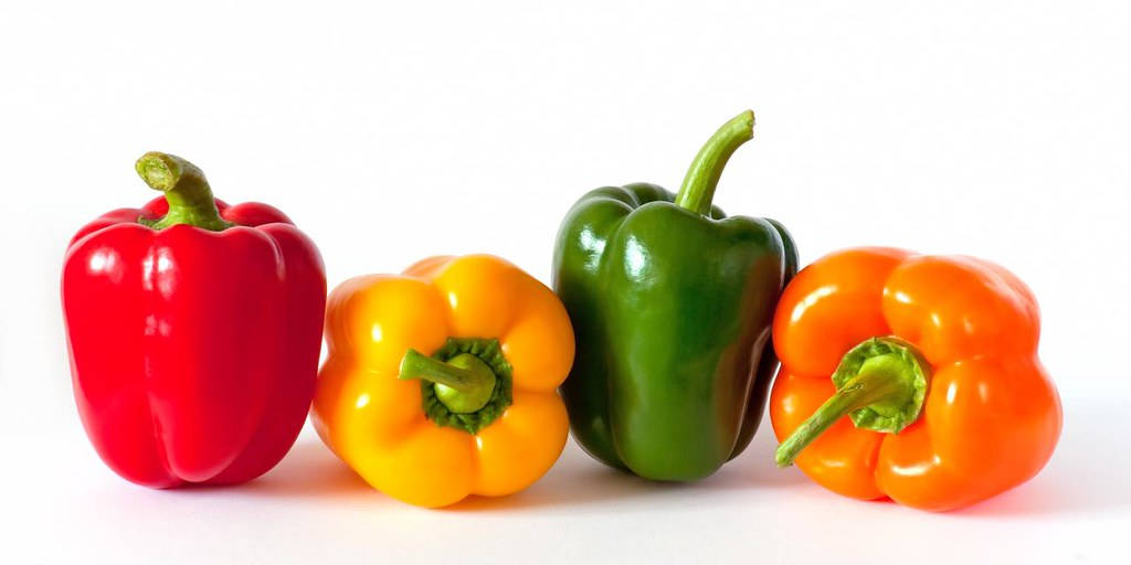 Fruits 桌布 壁紙 — 四個鮮豔的燈籠椒，紅色、黃色、綠色和橙色，整齊地排列在潔淨的白色背景上。