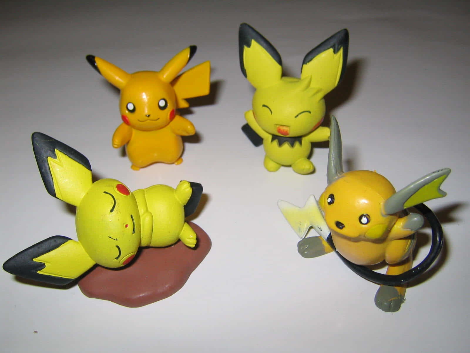 Pokemon Toys 桌布 壁紙 — 四個黃色皮卡丘和雷丘公仔在純白表面上擺出俏皮姿勢。