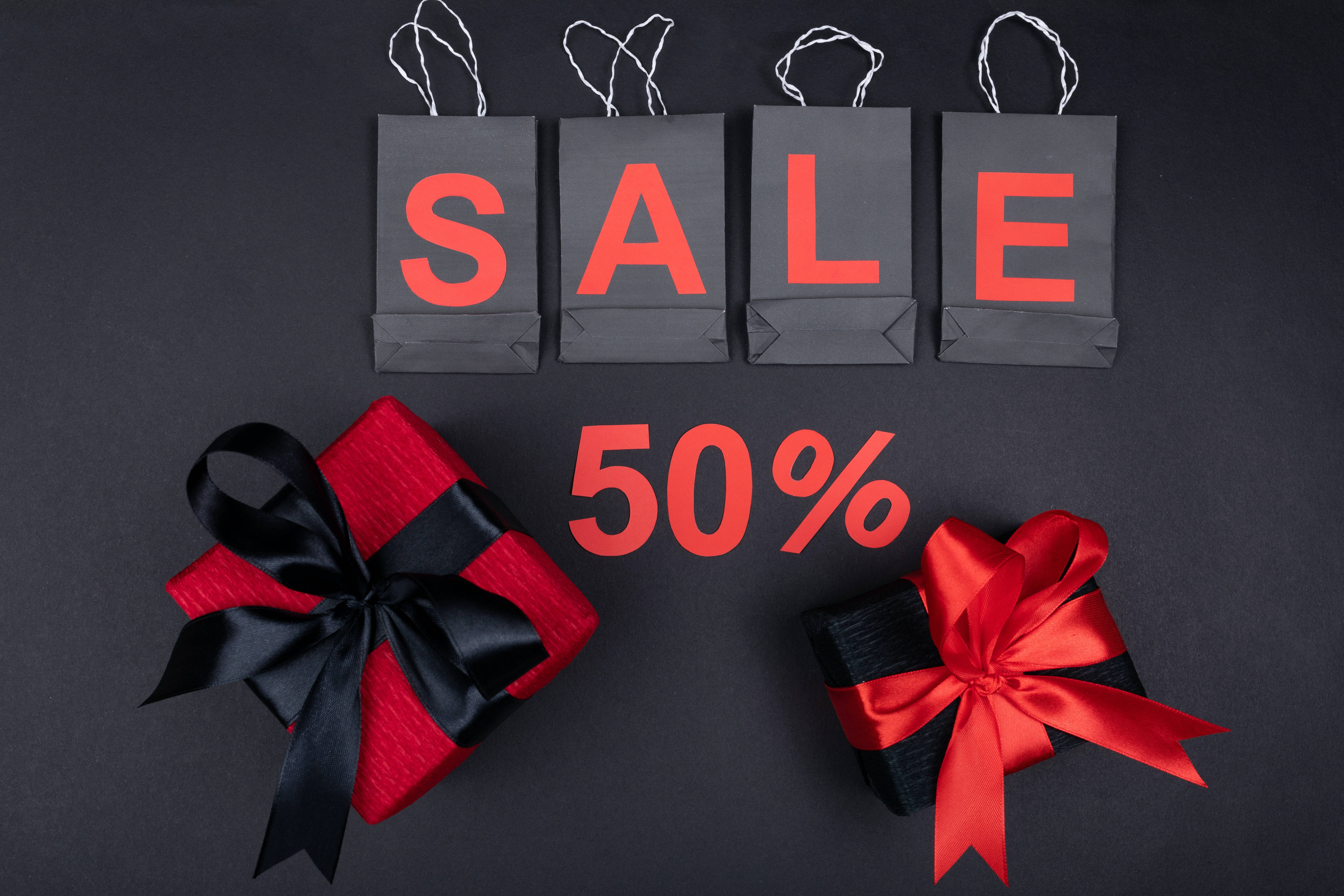 Shopping 桌布 壁紙 — 四個黑色紙袋用紅色字母拼出SALE，下方有兩個附有紅色和黑色蝴蝶結的包裝禮物，放在深灰色表面上。