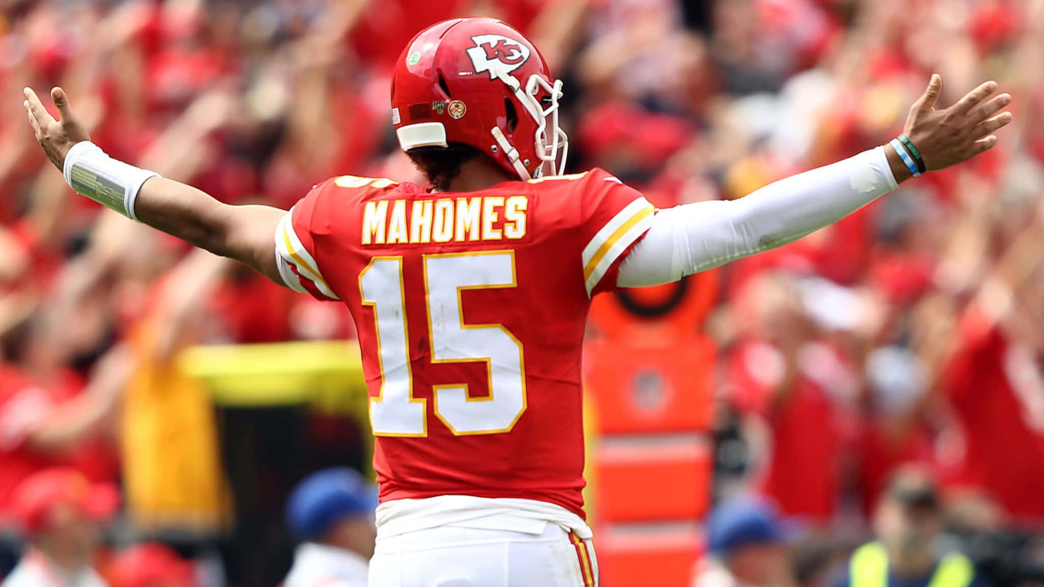 足球 桌布 壁紙 — 四分衛 Patrick Mahomes 身穿紅色15號球衣，在陽光照耀的足球場上張開雙臂慶祝。