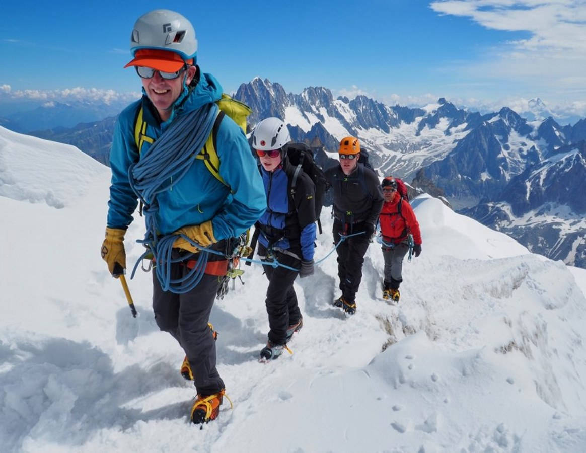 攀爬 桌布 壁紙 — 四名全副裝備的登山者在晴朗的藍天下穿越白雪覆蓋的山脊，遠處是鋸齒狀的山峰。