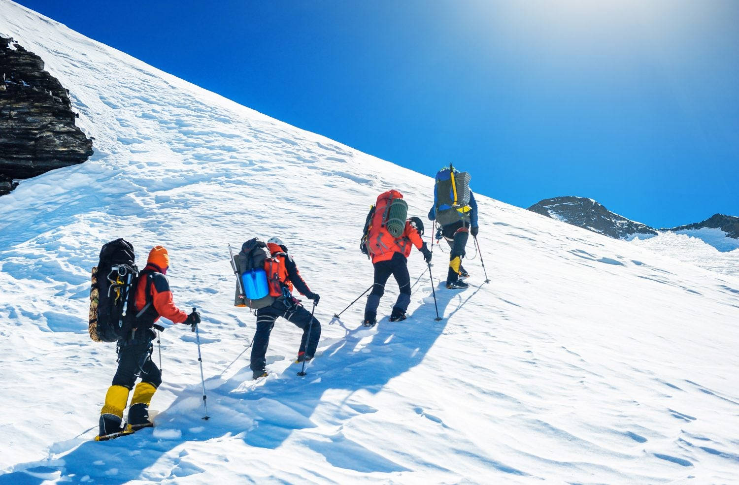 攀爬 桌布 壁紙 — 四名穿著鮮豔裝備的登山者在晴朗的藍天下攀登陡峭的雪山斜坡。