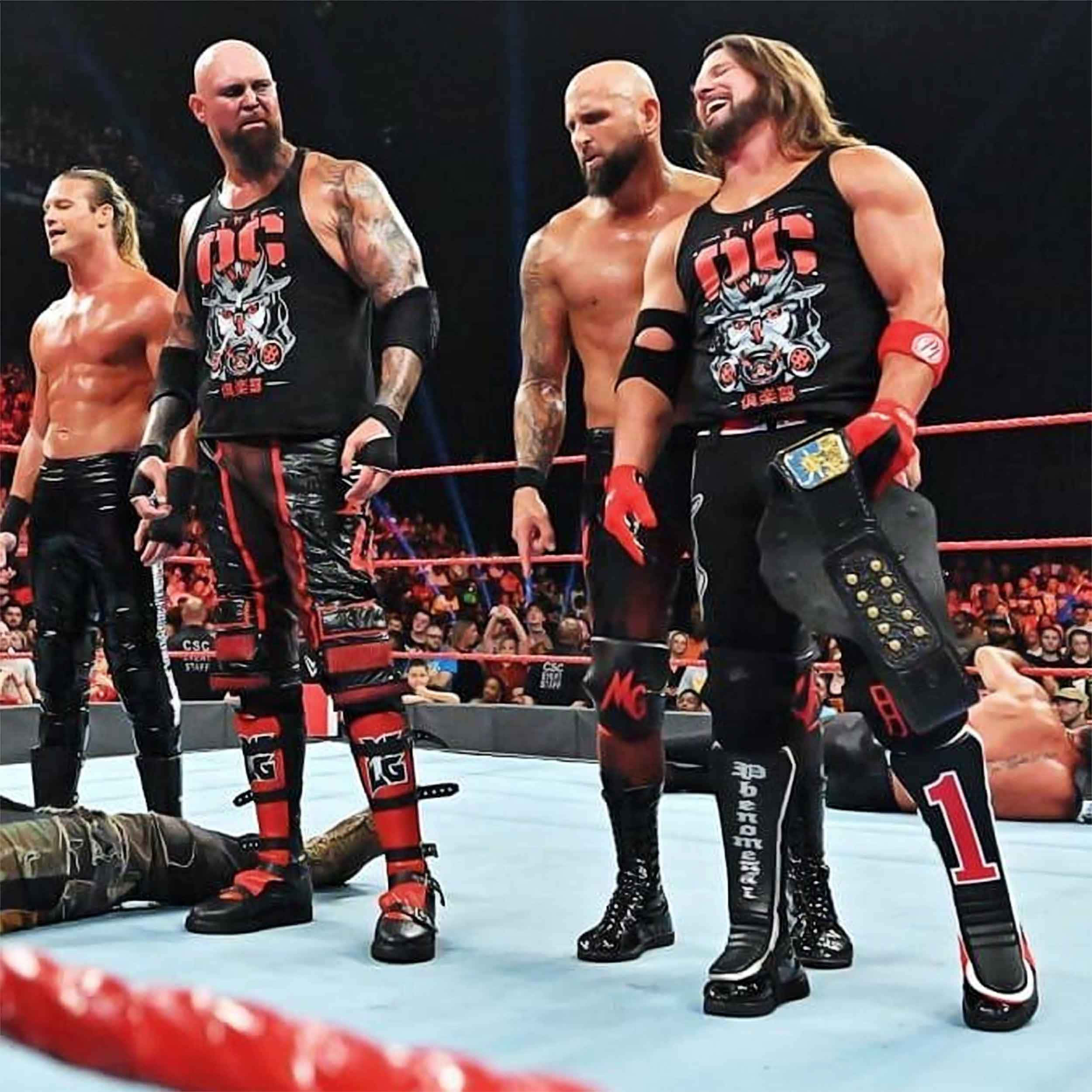 WWE 桌布 壁紙 — 四名肌肉發達的摔角手身穿黑色和紅色裝備，在擂台上勝利地站立，對手倒地，觀眾在他們身後歡呼。