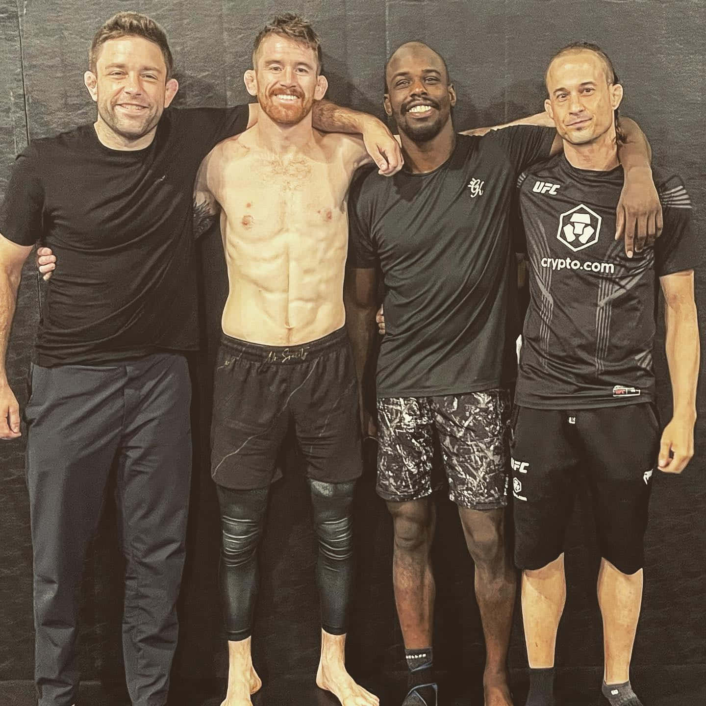 MMA 桌布 壁紙 — 四名肌肉發達的男子身穿運動服，互相搭著肩膀，在深色紋理牆前合影。