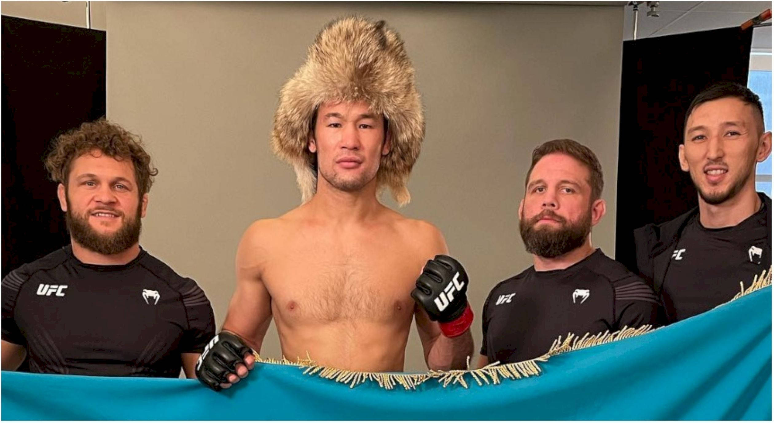 UFC 桌布 壁紙 — 四名身穿UFC裝備的男子在室內與一面藍旗合影，其中一人戴著大毛帽。