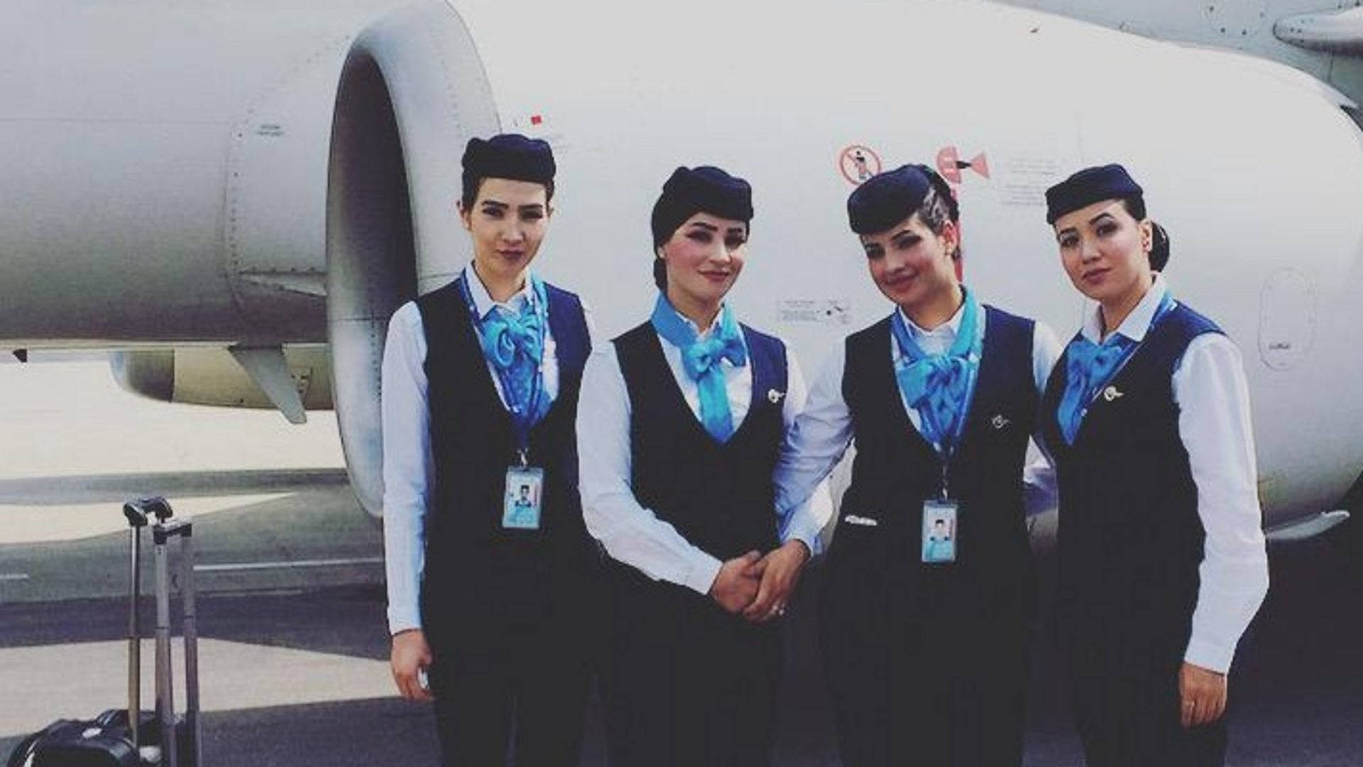 Airport 桌布 壁紙 — 四名身穿制服的空姐在停機坪上自信地擺姿勢，旁邊是一台大型飛機引擎。