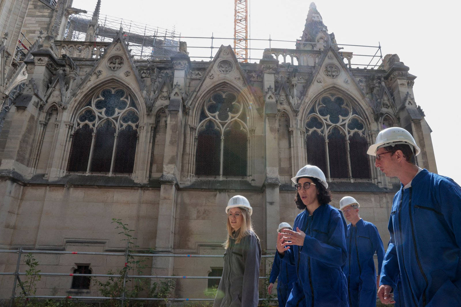 Notre Dame 桌布 壁紙 — 四名身穿藍色制服和白色安全帽的建築工人在燦爛的陽光下站在巴黎聖母院的哥德式立面前。