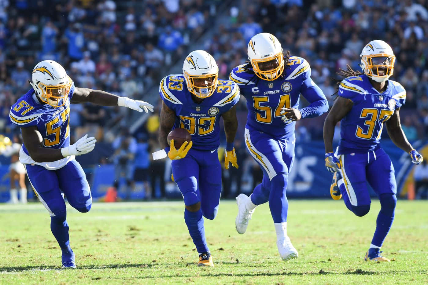 NFL 桌布 壁紙 — 四名身穿藍色和金色球衣的 Chargers 美式足球員在陽光明媚的球場上全力衝刺，其中一人持球。