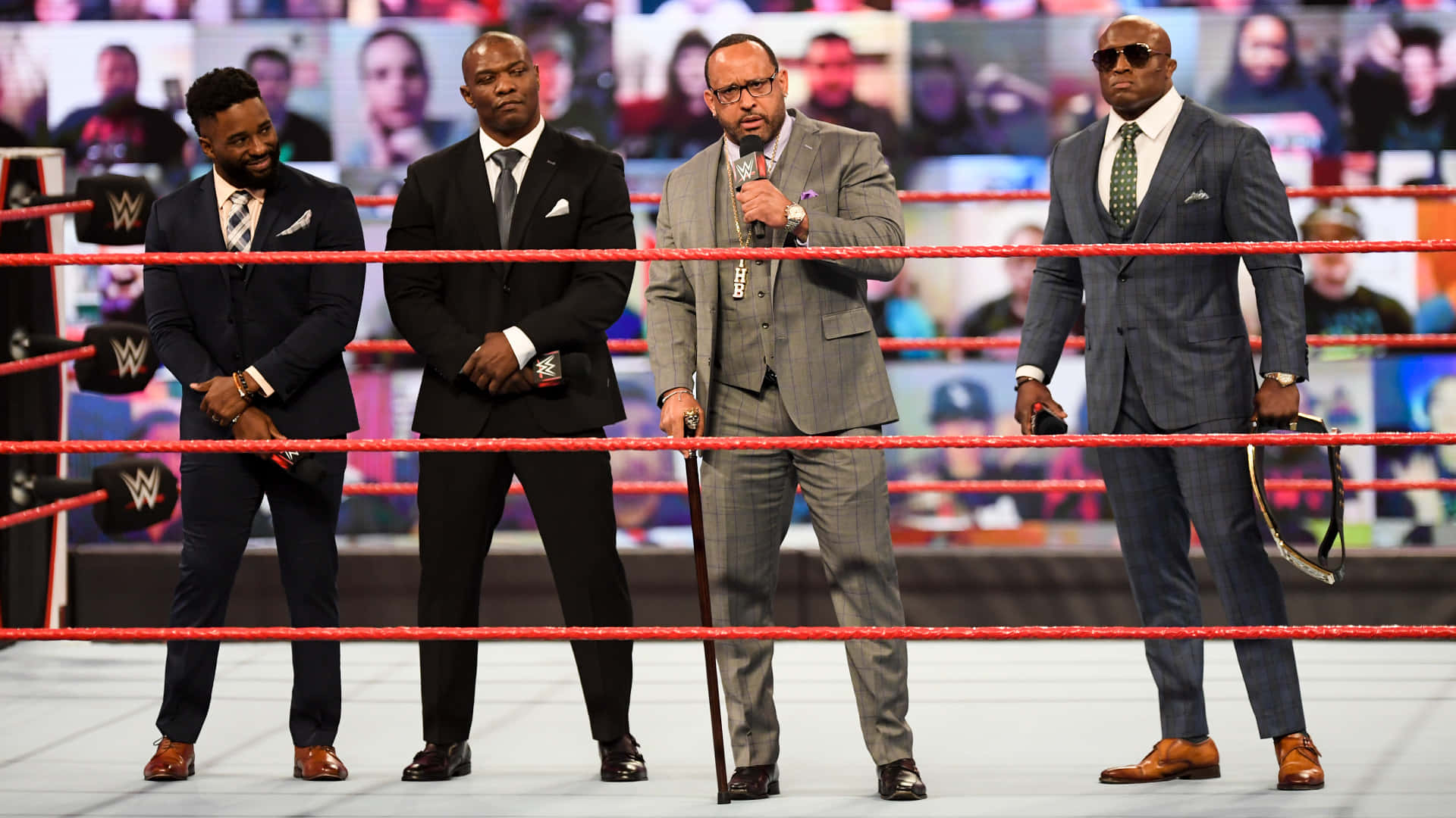 WWE 桌布 壁紙 — 四名身穿西裝的男子站在WWE摔角擂台內，擂台有紅色繩索和角柱上的WWE標誌。