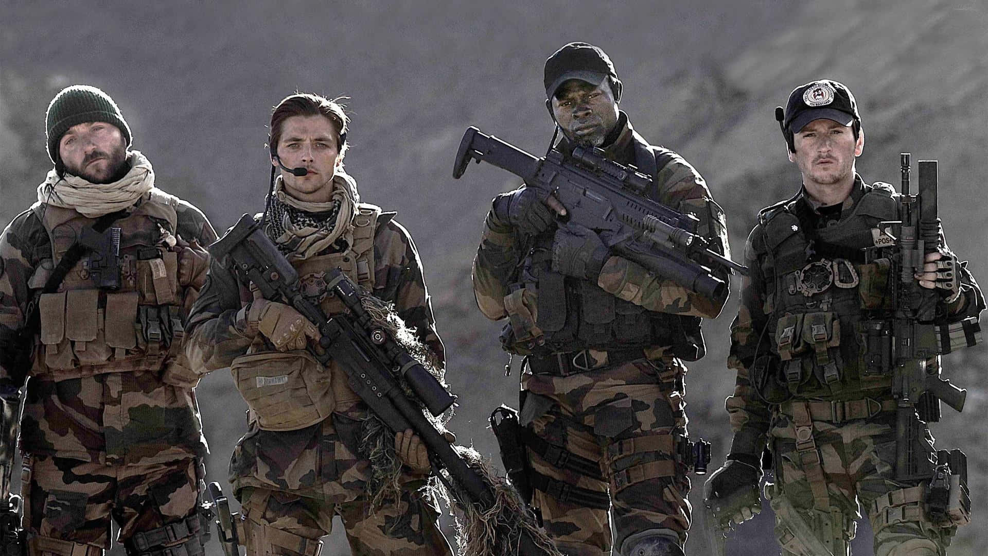  壁紙 — 四名身穿迷彩裝備的士兵站在崎嶇的山地地形中，手持步槍，表情嚴肅。