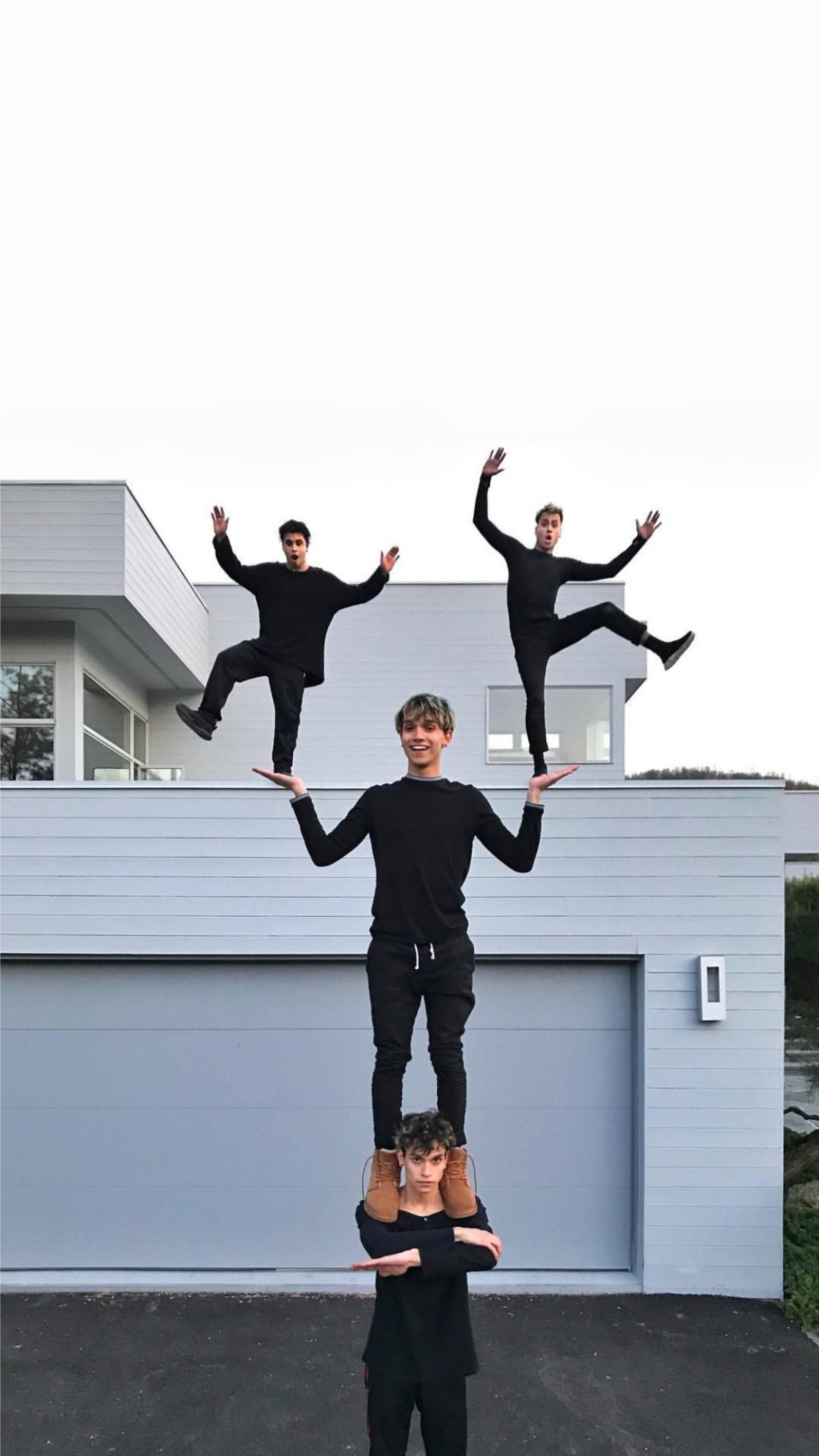Dobre 桌布 壁紙 — 四名身穿黑色服裝的年輕男子在現代灰色房屋外伸出雙臂形成人體金字塔。