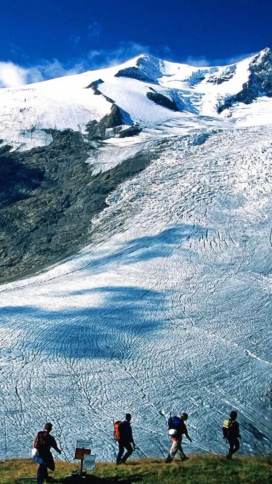 Climbing 桌布 壁紙 — 四名遠足者在晴朗的藍天下，穿越一座高聳積雪山脈下的廣闊冰川。