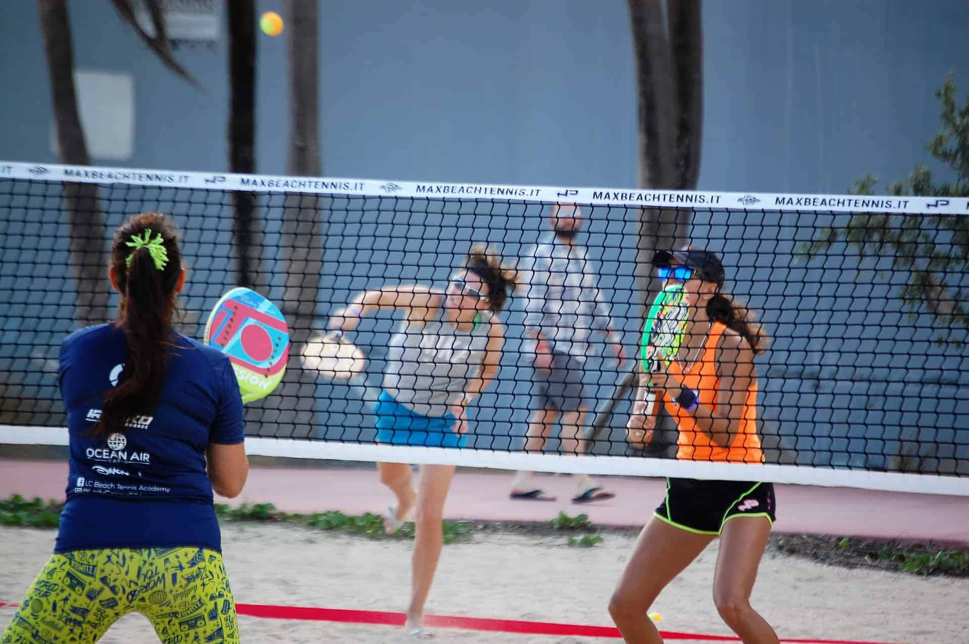 Beach Tennis 桌布 壁紙 — 四名選手在沙地球場上激烈進行沙灘網球比賽，背景有棕櫚樹和網。