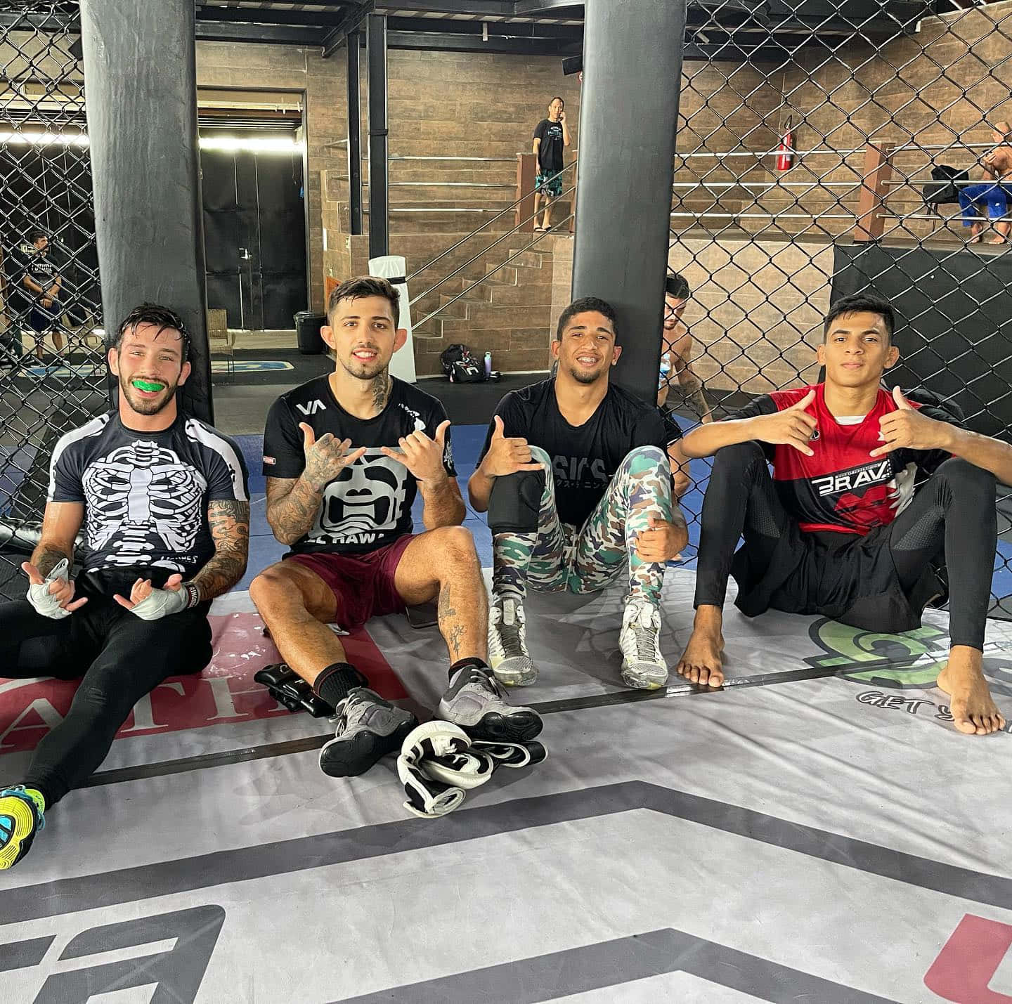 MMA 桌布 壁紙 — 四名面帶微笑的男性拳手身穿MMA裝備，在健身房的籠墊上自信地擺姿勢。