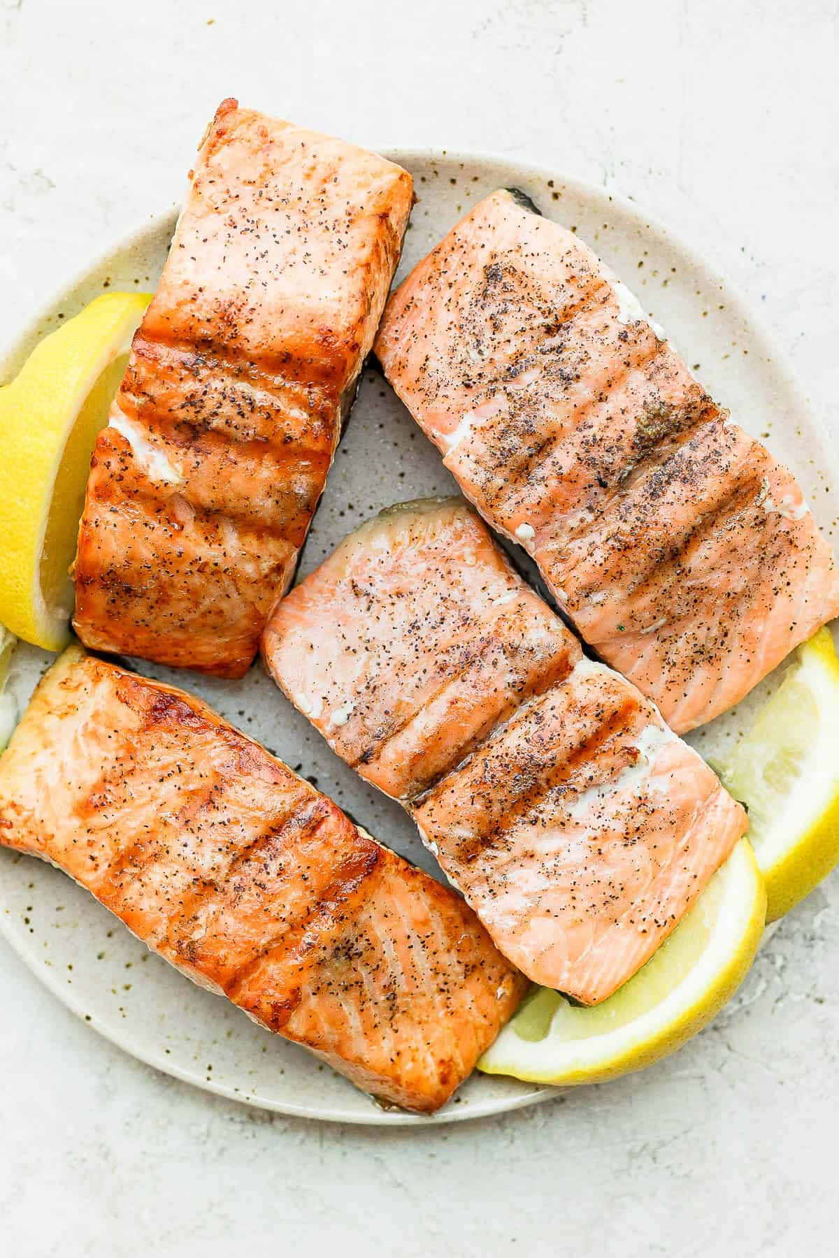 Salmon 桌布 壁紙 — 四塊帶有烤痕和黑胡椒的烤鮭魚排放在有斑點的盤子上，旁邊有檸檬角。