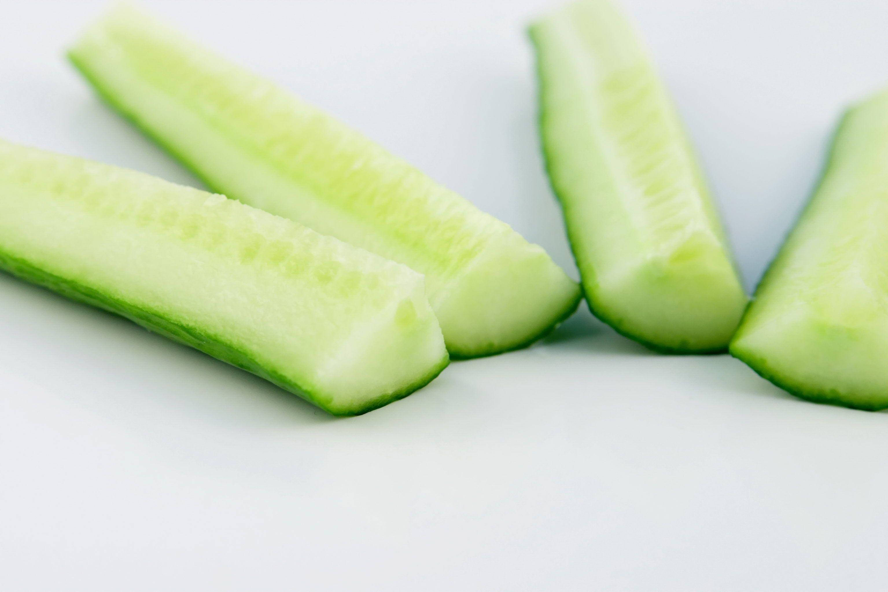 sliced 桌布 壁紙 — 四塊清脆的小黃瓜片對角排列在明亮的白色表面上，帶有柔和陰影。