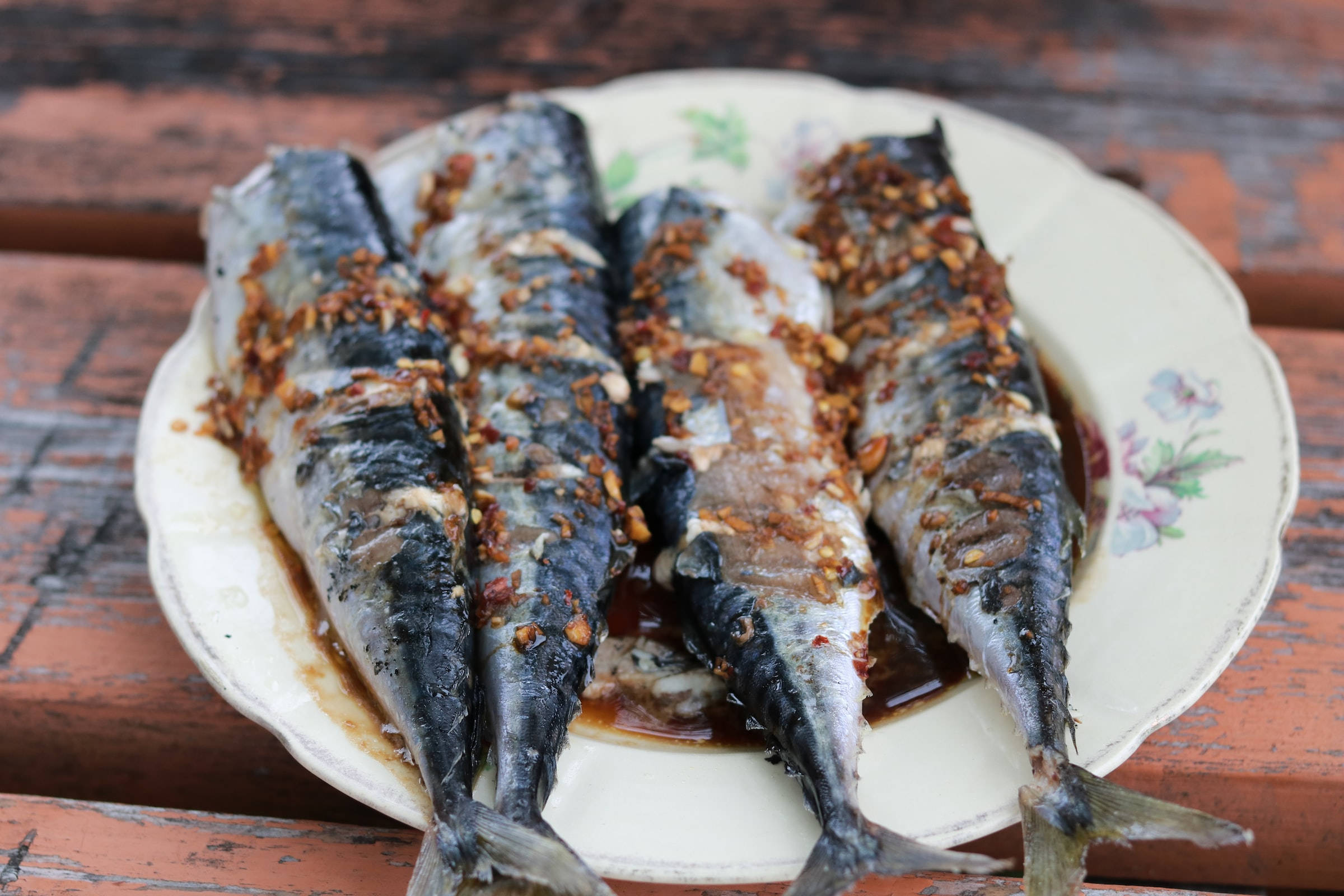 魚 桌布 壁紙 — 四塊烤鯖魚柳配上脆蒜和醬油，放在花紋盤上，置於經風化的木桌上。