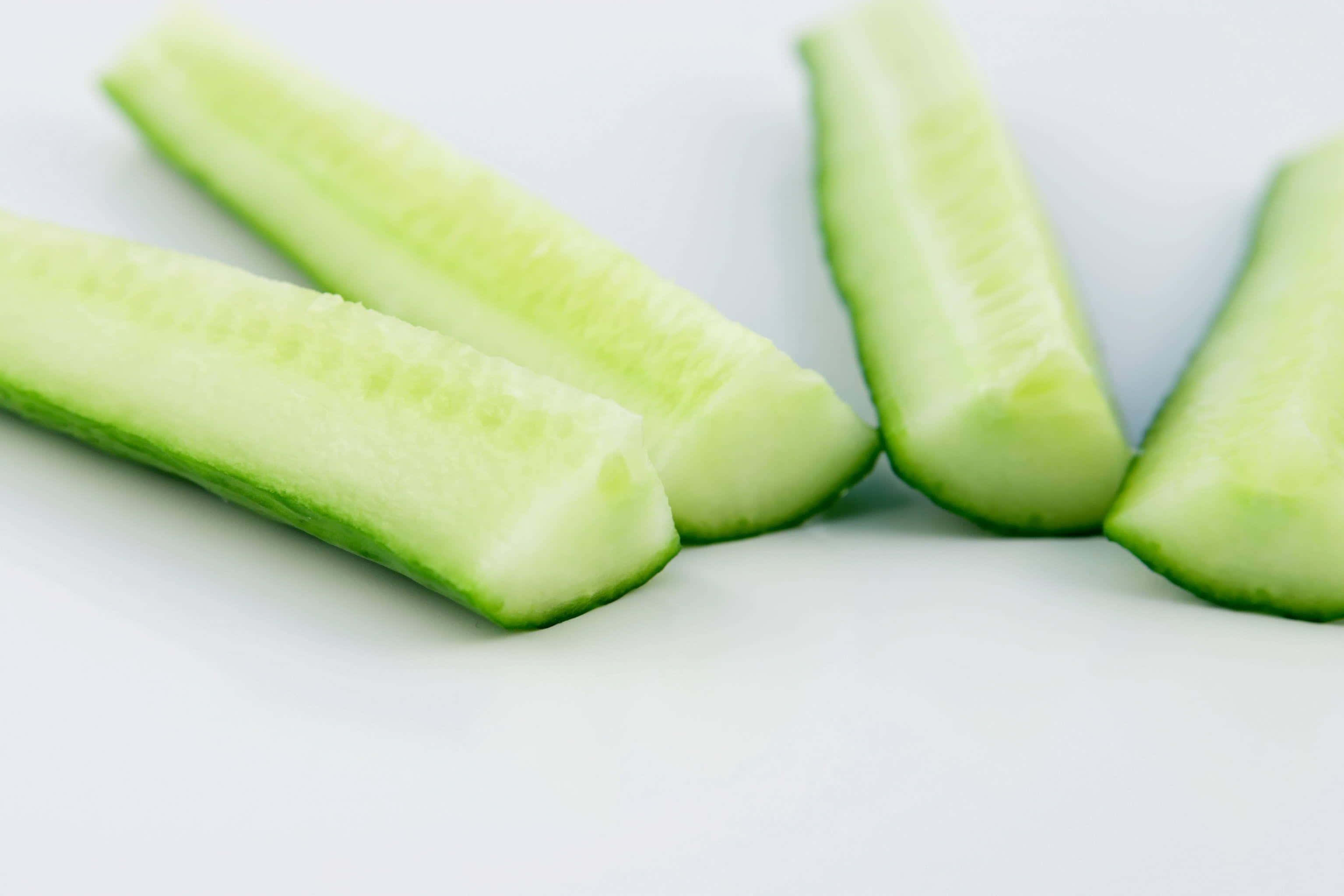 cucumber 桌布 壁紙 — 四塊爽脆黃瓜片對角排列在明亮的白色表面上，帶有柔和陰影。