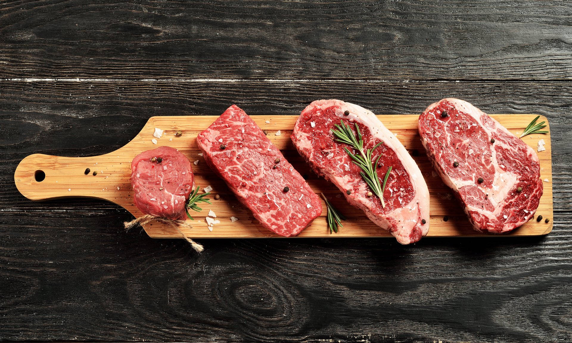 meat 桌布 壁紙 — 四塊生牛肉搭配迷迭香和鹽，放置在木板上，背景為深色鄉村風格木材。