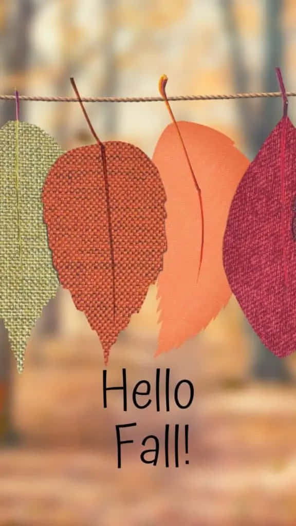 Simple Fall 桌布 壁紙 — 四塊秋色調的布料葉子掛在繩子上，背景是模糊的森林，帶有'Hello Fall!'文字。