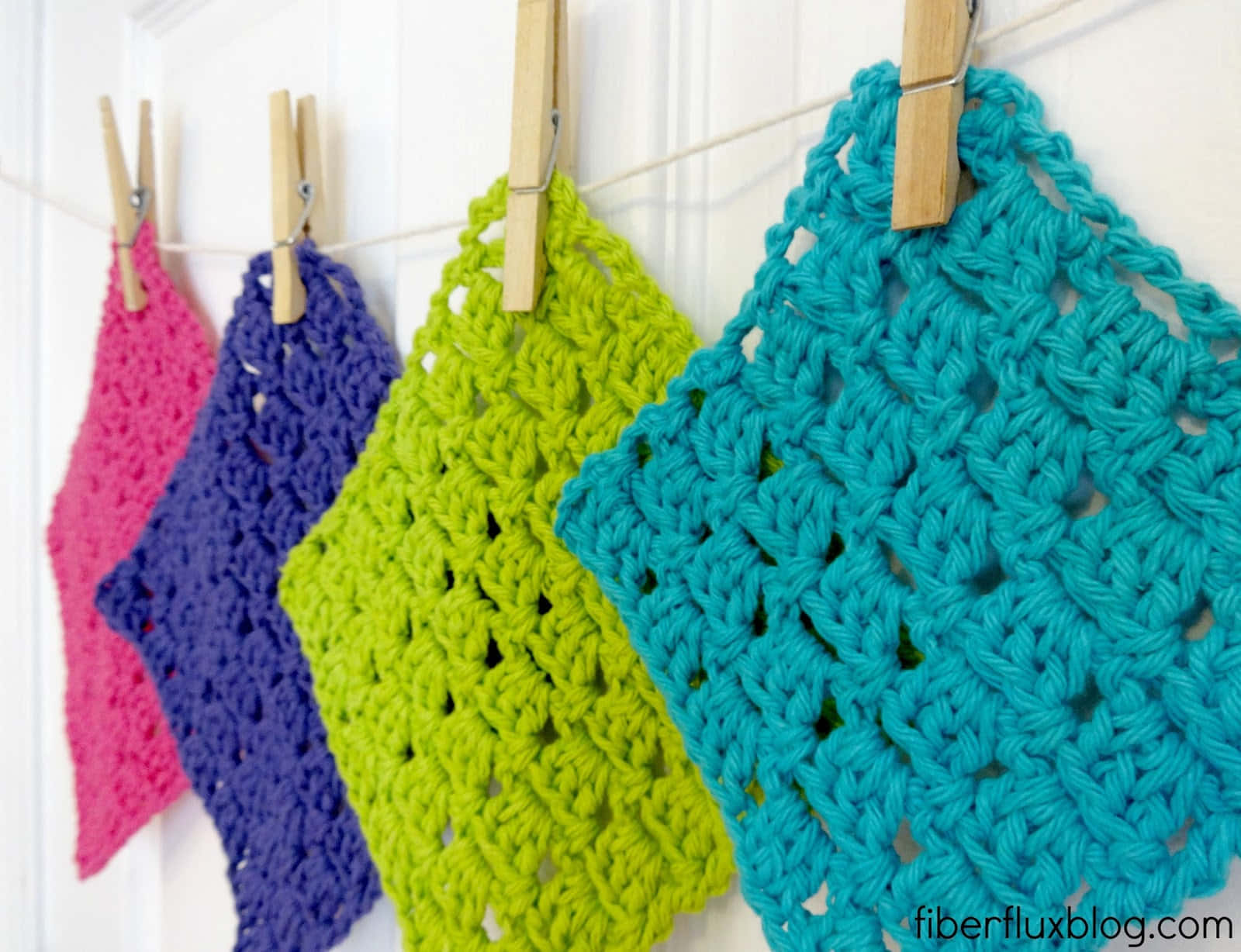 Crochet 桌布 壁紙 — 四塊色彩鮮豔的鉤針編織洗碗布用木衣夾掛在白色繩子上，背景是鑲板牆。