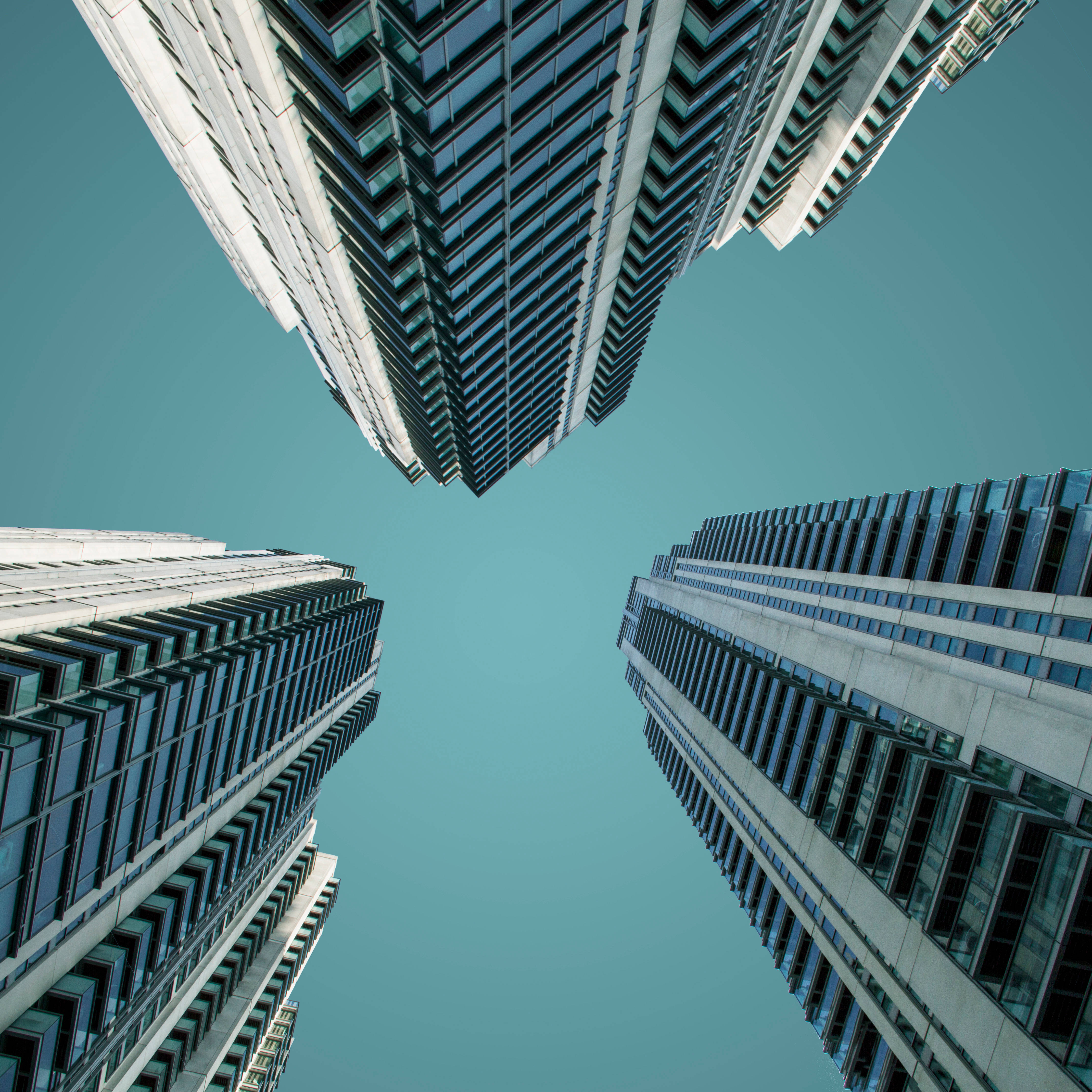 Skyscraper 桌布 壁紙 — 四座高聳的摩天大樓向清澈的青綠色天空匯聚，形成戲劇性的低角度城市景觀。