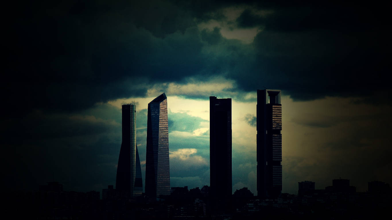 Madrid 桌布 壁紙 — 四座高聳的摩天大樓在戲劇性的暴風雨天空和發光的雲層襯托下，呈現出黑暗的剪影。