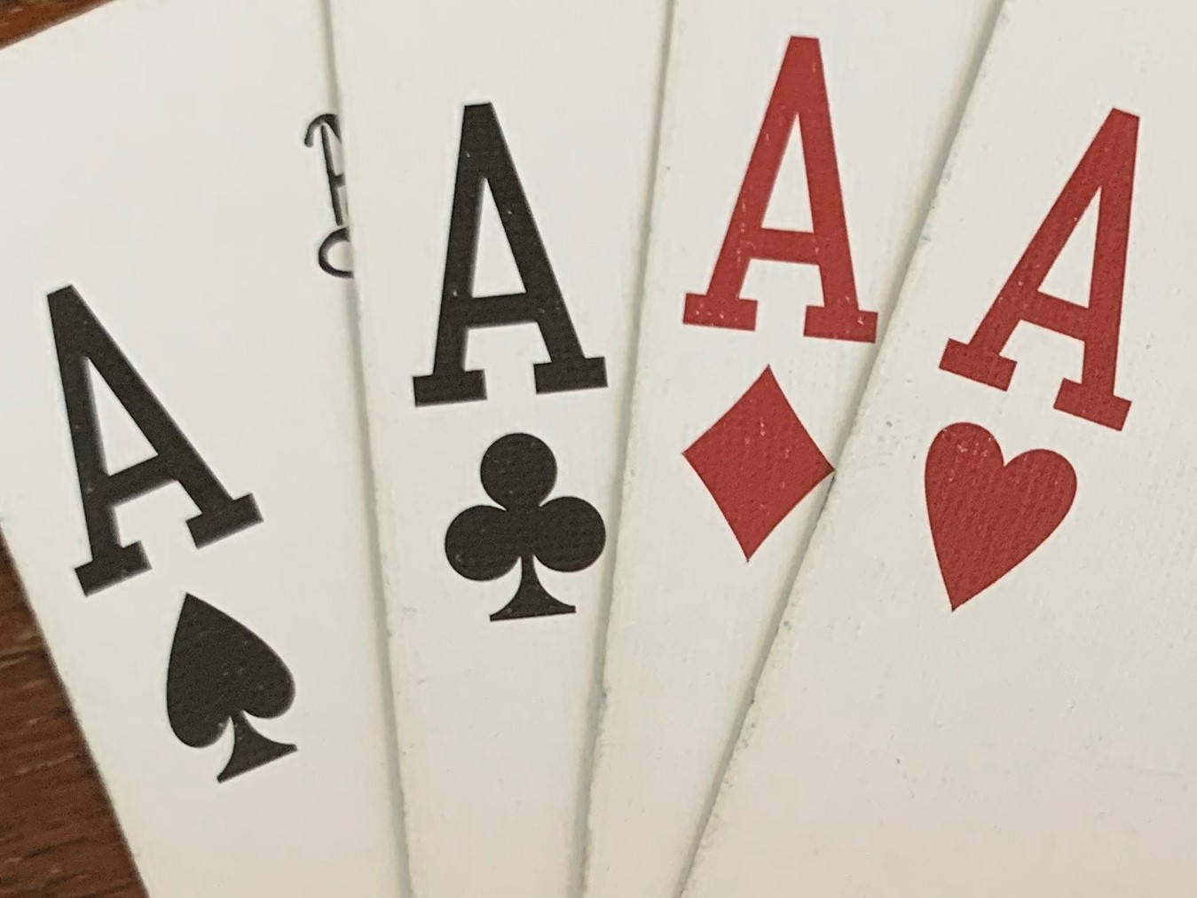 Playing Cards 桌布 壁紙 — 四張Ace撲克牌扇形展開，顯示黑桃、梅花、方塊和紅心，置於有紋理的白色表面上。