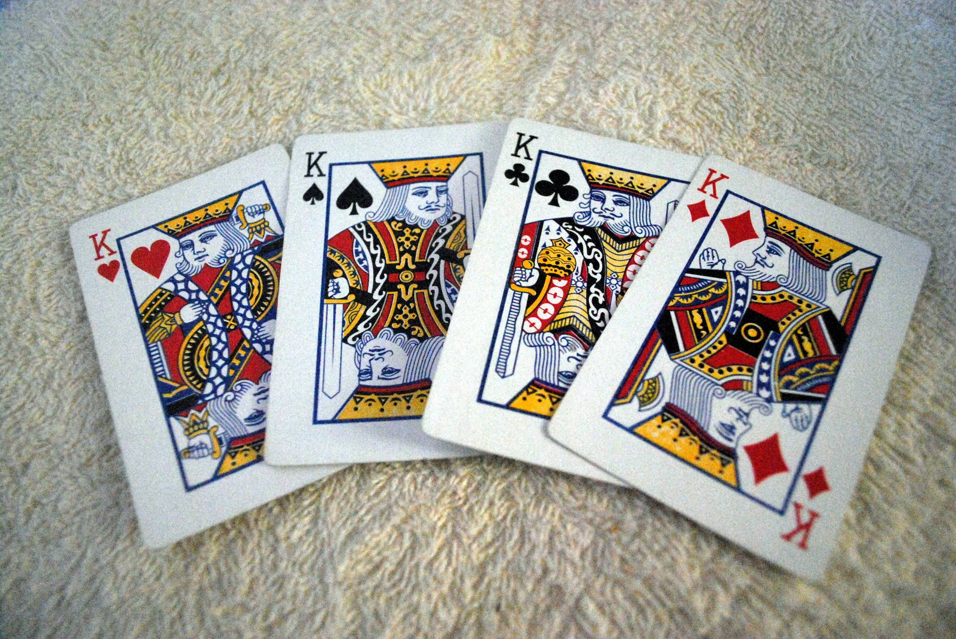 Playing Cards 桌布 壁紙 — 四張皇家撲克牌，紅心、黑桃、梅花、方塊的K，攤開在柔軟有紋理的米色毛巾上。