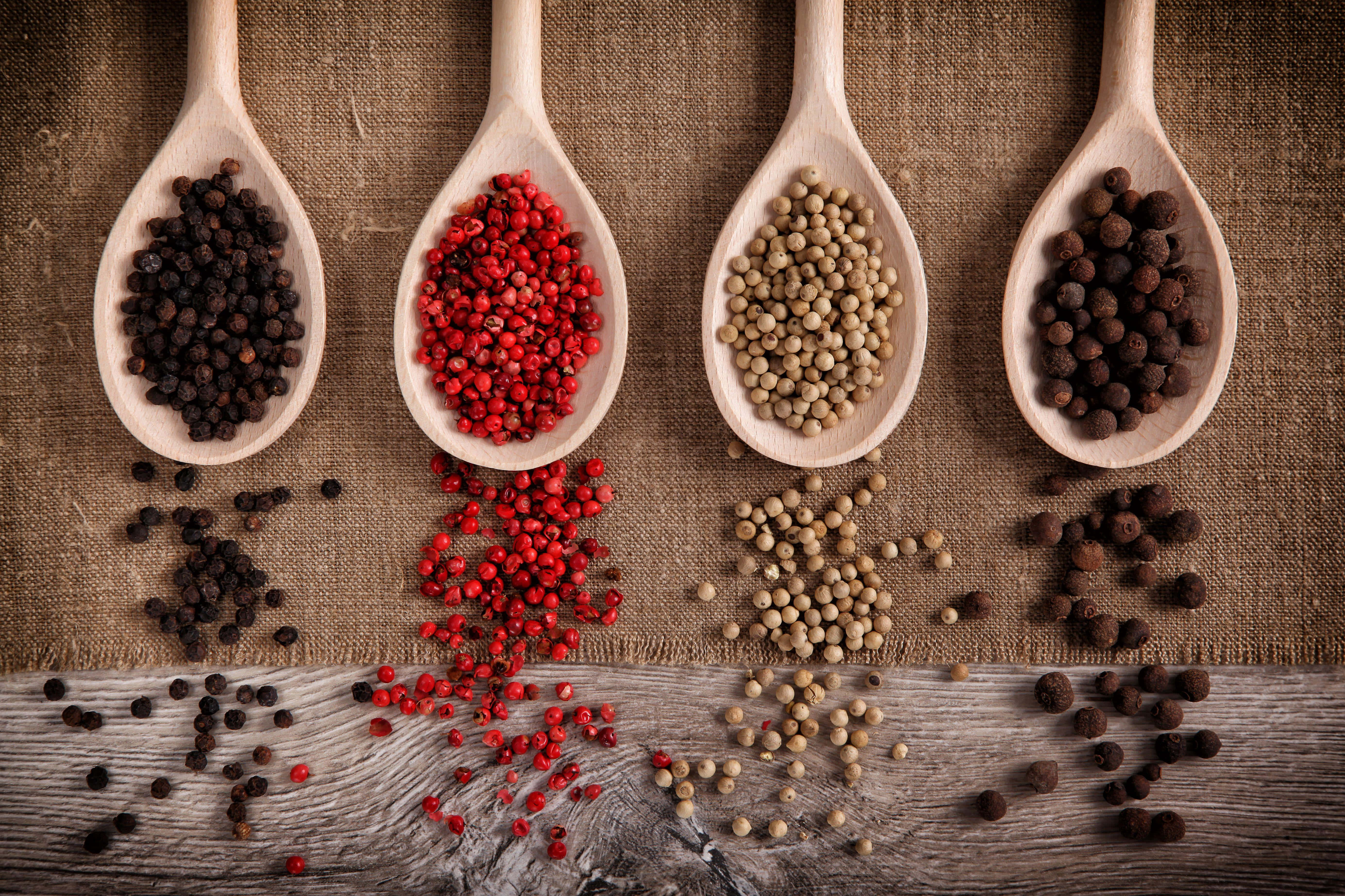 Spices 桌布 壁紙 — 四把木匙盛載黑、紅、白和棕色胡椒粒，排列在麻布和木頭上，並散落著香料。