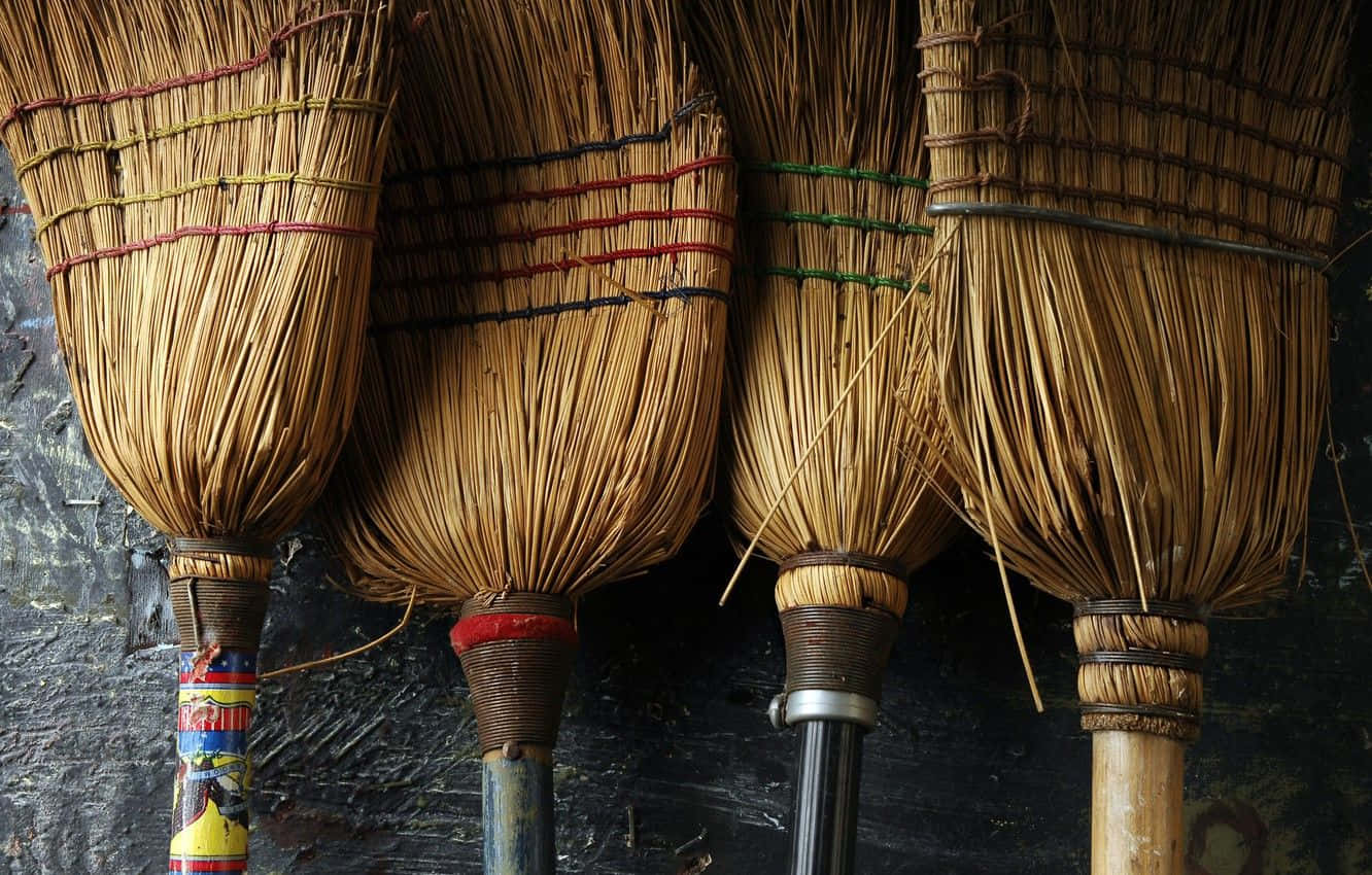 Broom 桌布 壁紙 — 四把鄉村風格的掃帚，帶有編織稻草刷毛和彩色綁帶，掛在深色紋理牆上。