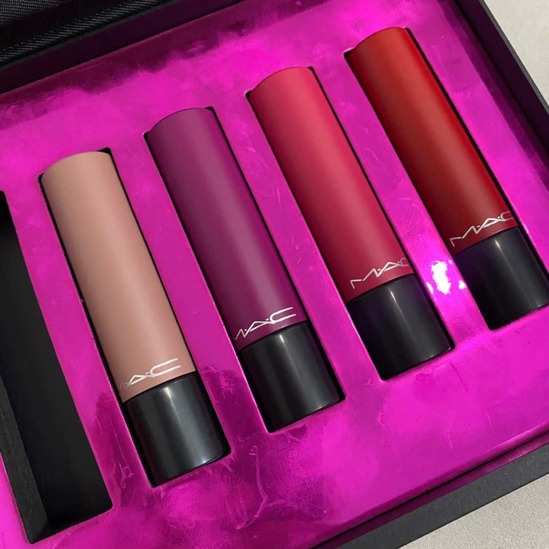 Mac Cosmetics 桌布 壁紙 — 四支MAC唇膏，色調包括裸色、紫紅色、玫瑰色和紅色，放置在一個充滿活力的粉紅色紋理盒子中。