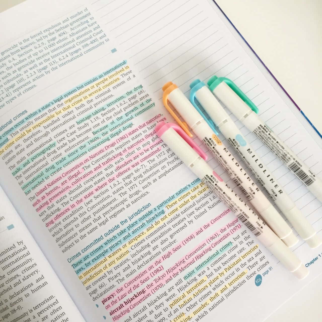 Highlight 桌布 壁紙 — 四支色彩繽紛的Mildliner螢光筆放在一本打開的教科書頁面上，頁面有被標示的法律文字。