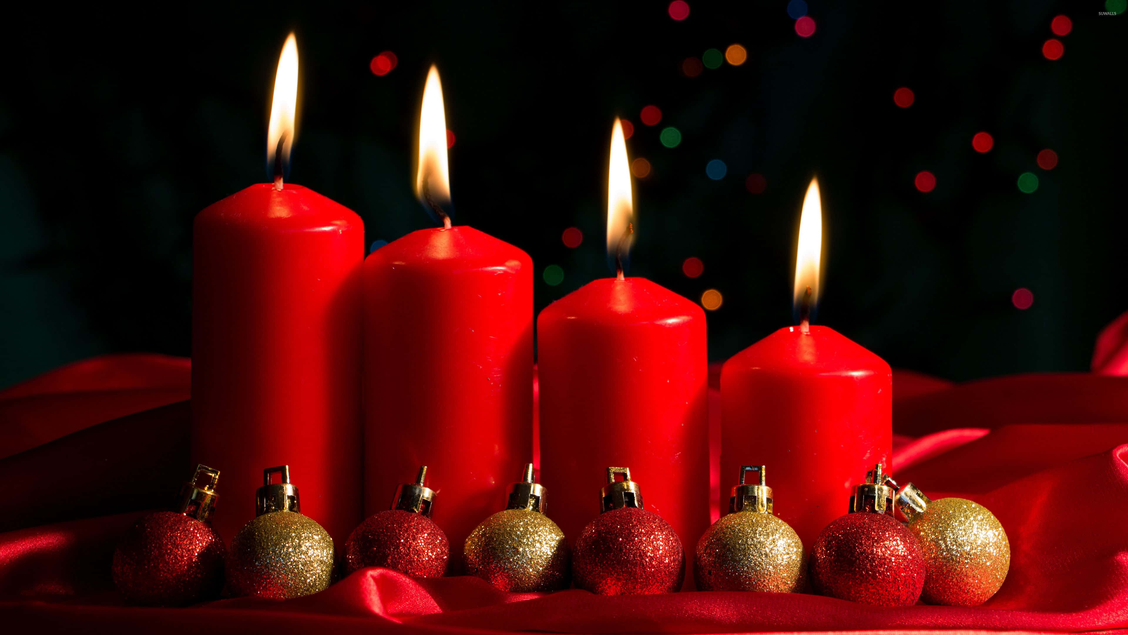 Advent 桌布 壁紙 — 四支點燃的紅色蠟燭在深色散景背景下，在華麗的紅色布料上閃爍的紅色和金色裝飾品旁邊溫暖地發光。