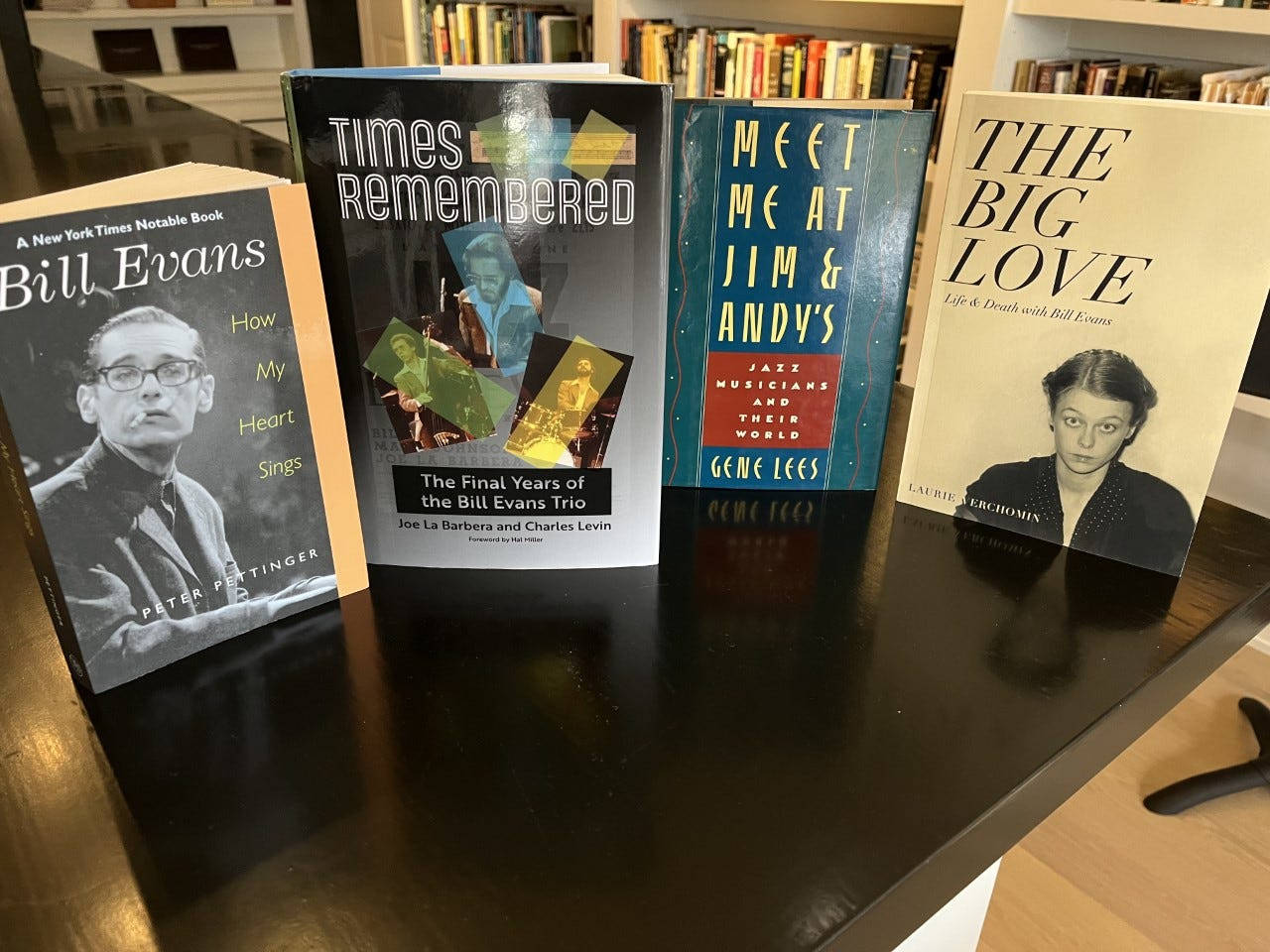 Library 桌布 壁紙 — 四本關於比爾·埃文斯的爵士傳記書籍放在一張深色木桌上，背景是書架。